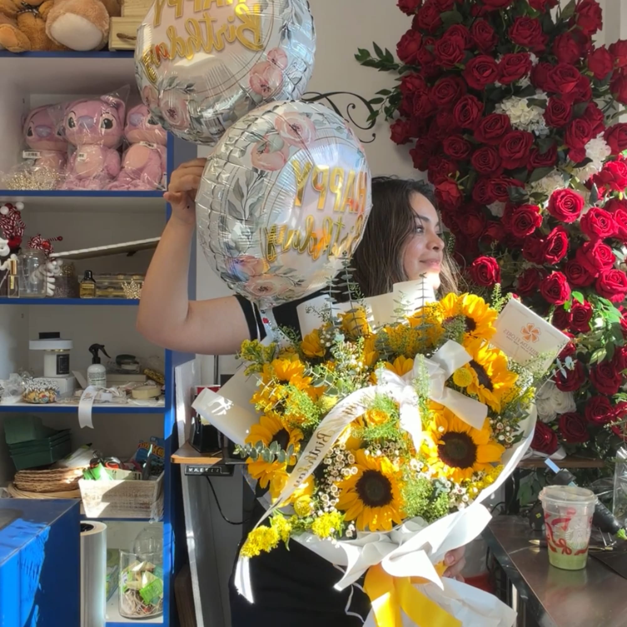 Woman holding a sunflower bouquet and two birthday balloons