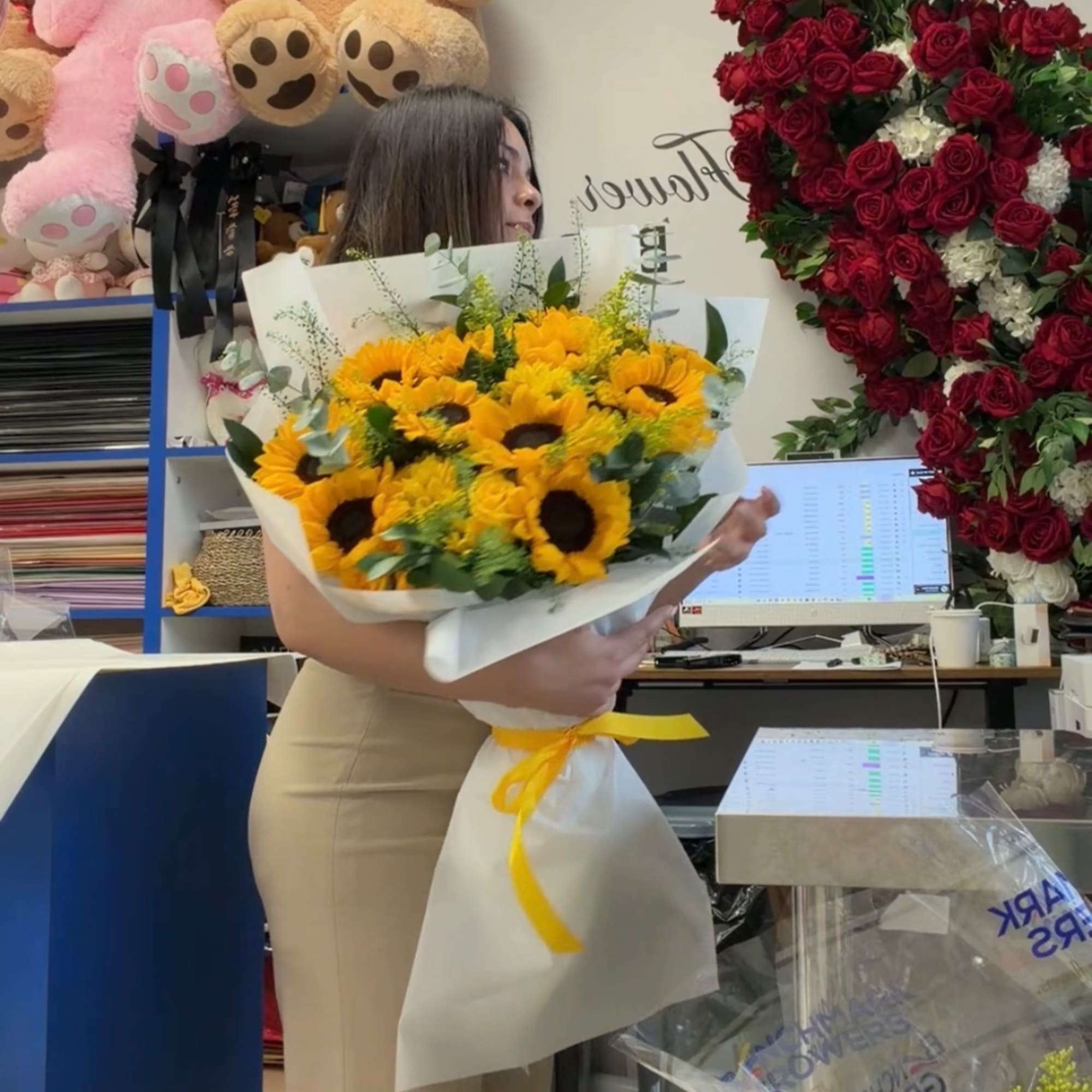 Woman holding a bouquet of yellow sunflowers wrapped in white paper with a yellow ribbon