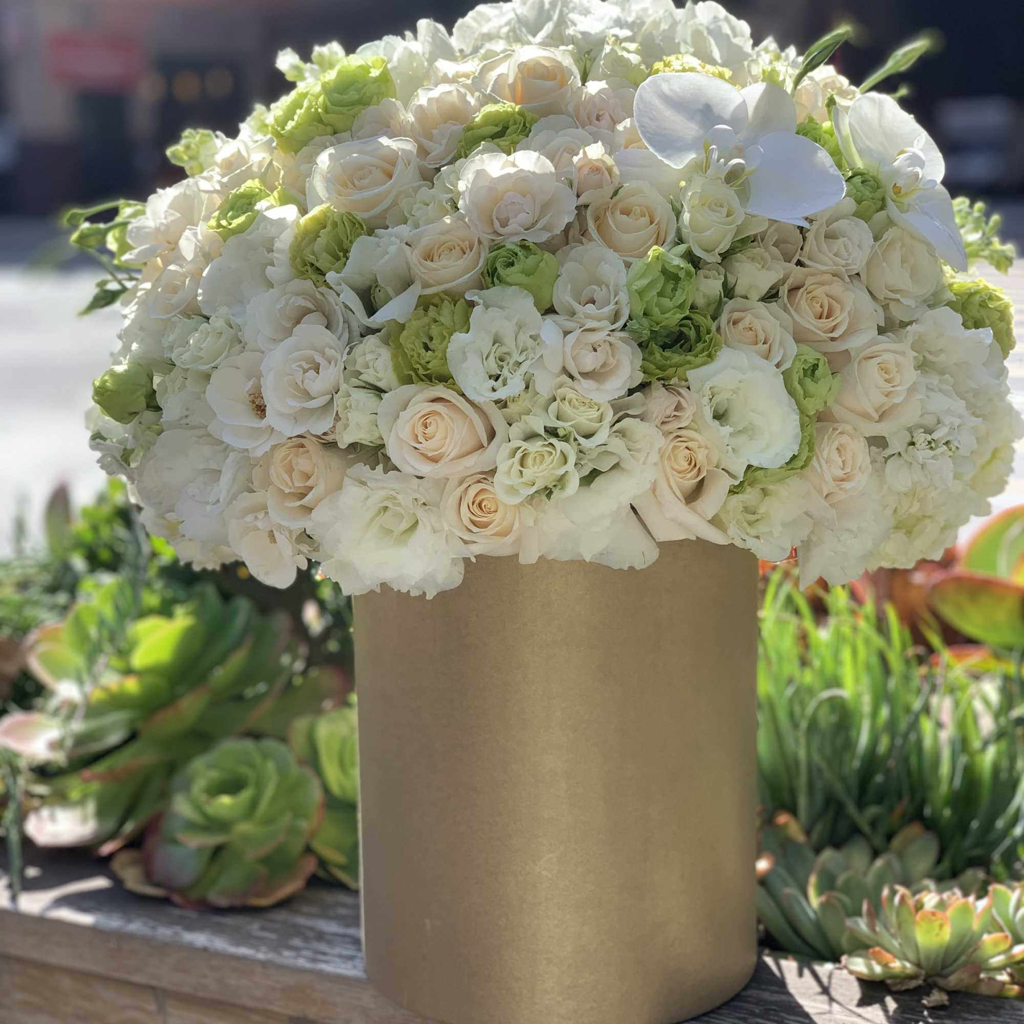 Large white and cream floral arrangement in a gold vase