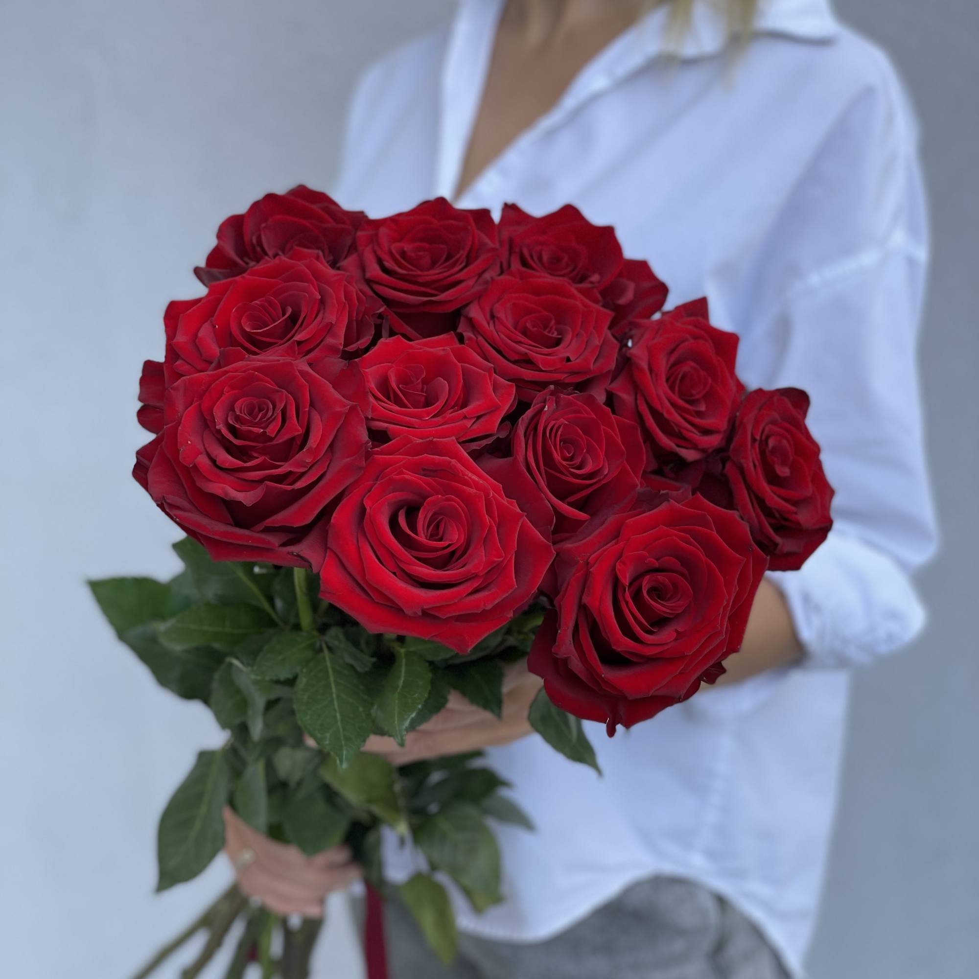 Bouquet of red roses held by a person in a white shirt