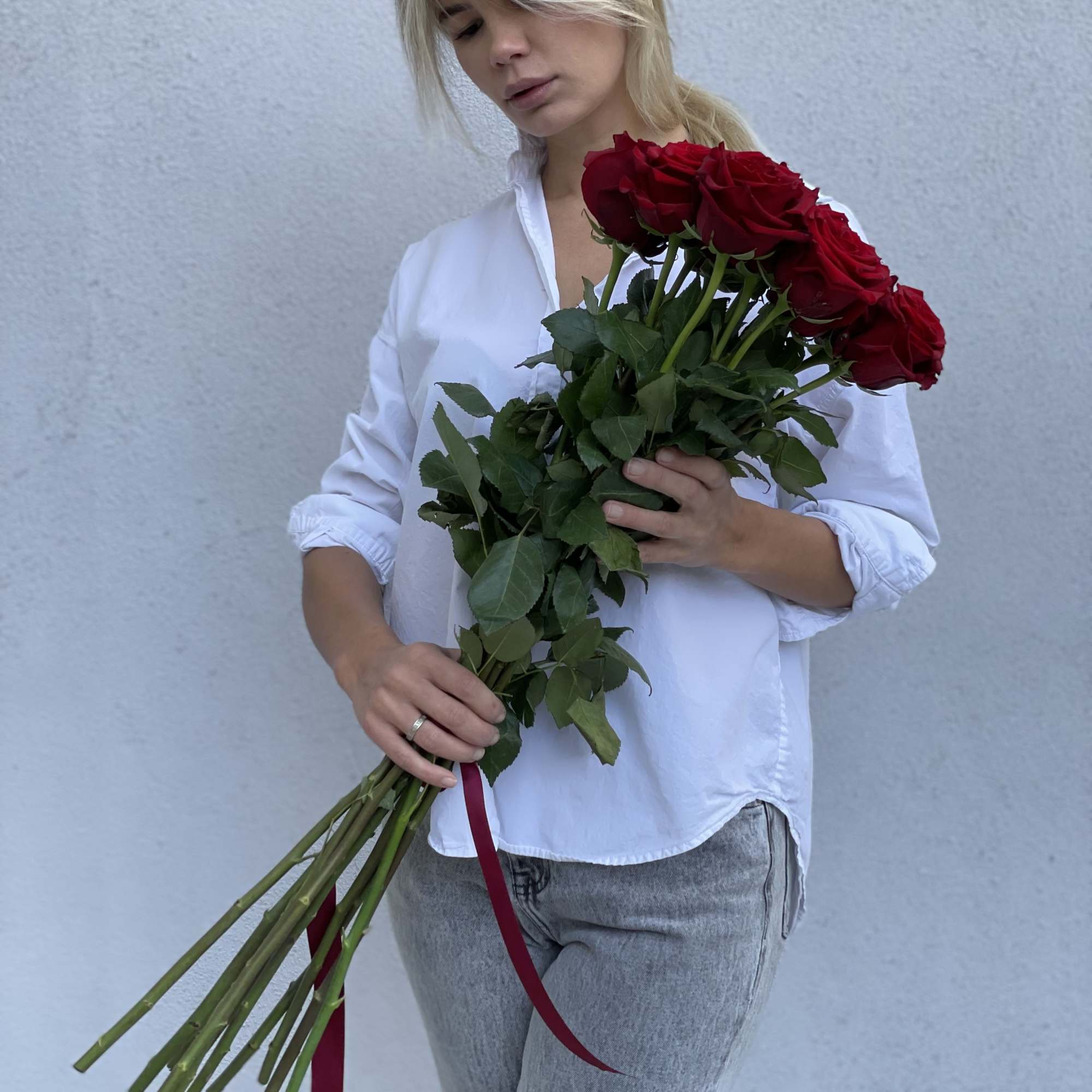Woman holding a long-stem bouquet of red roses with a ribbon