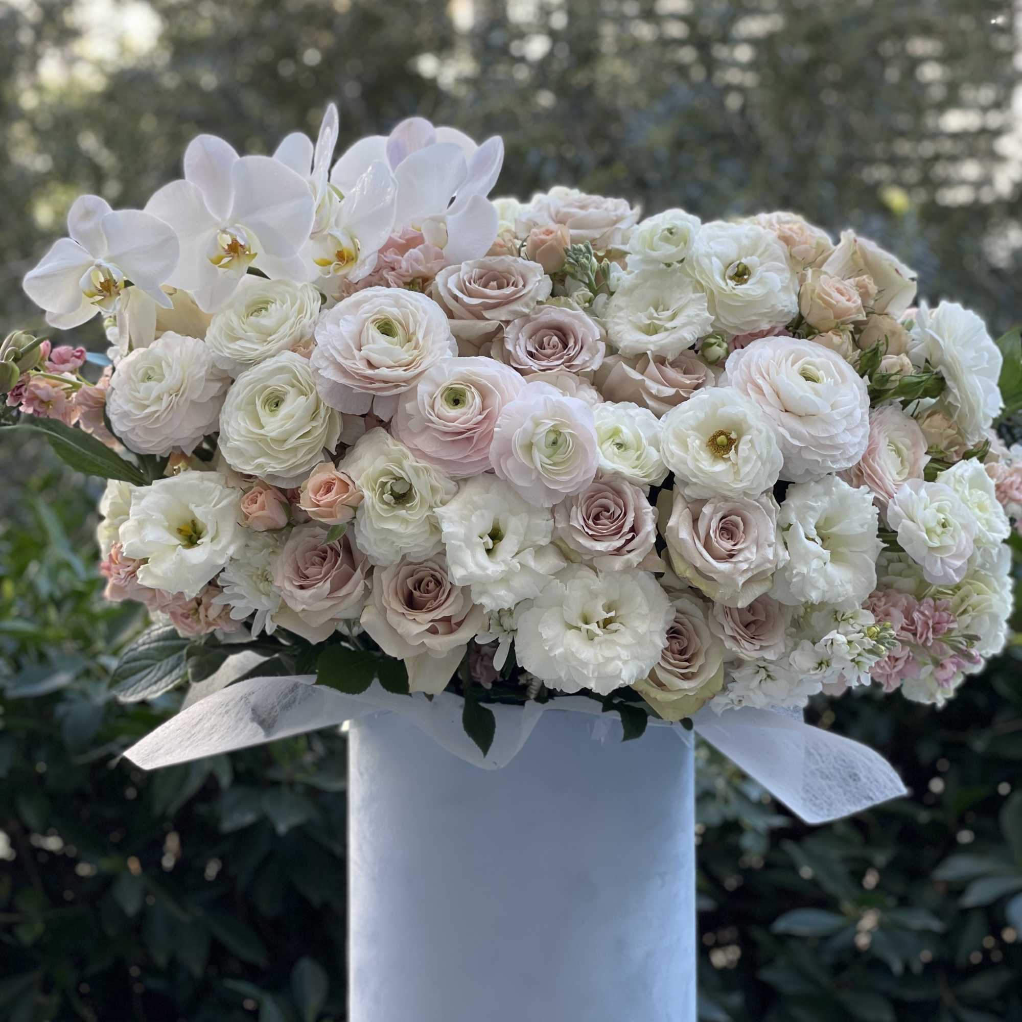 Large pastel bouquet of roses, ranunculus, and white orchids in a white box