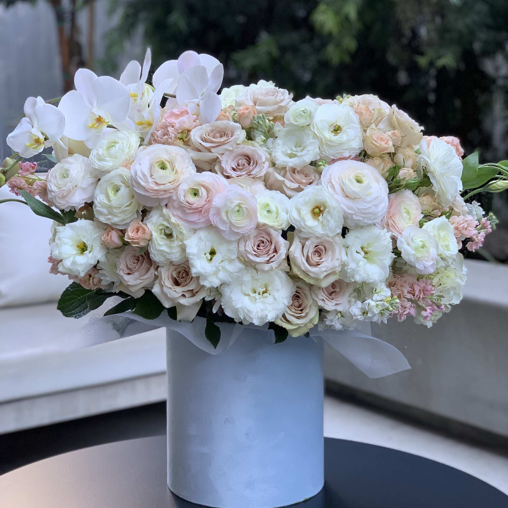 Blush and white floral arrangement in a pale blue box with orchids and roses