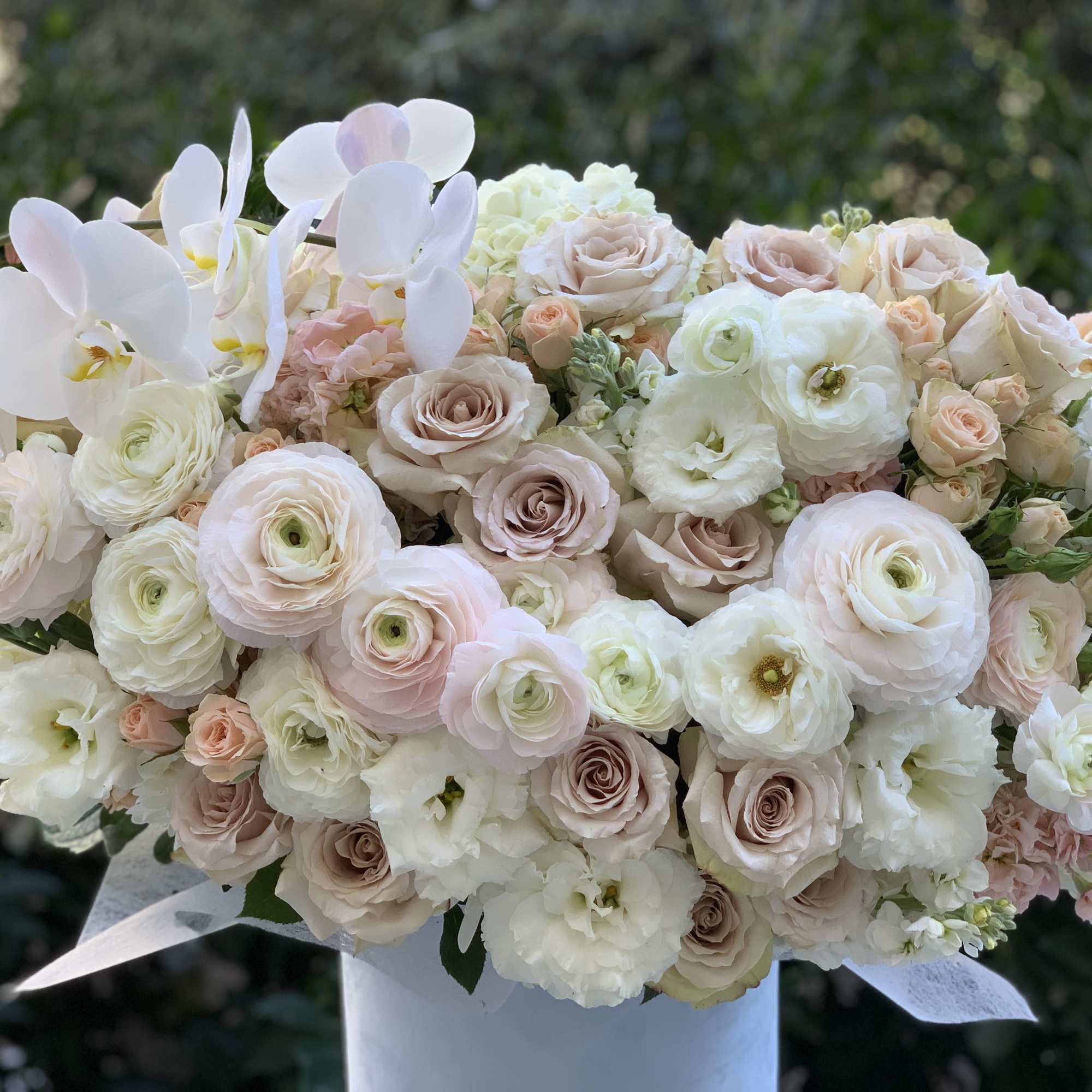 Blush and white bouquet with orchids, roses, and ranunculus in a white vase