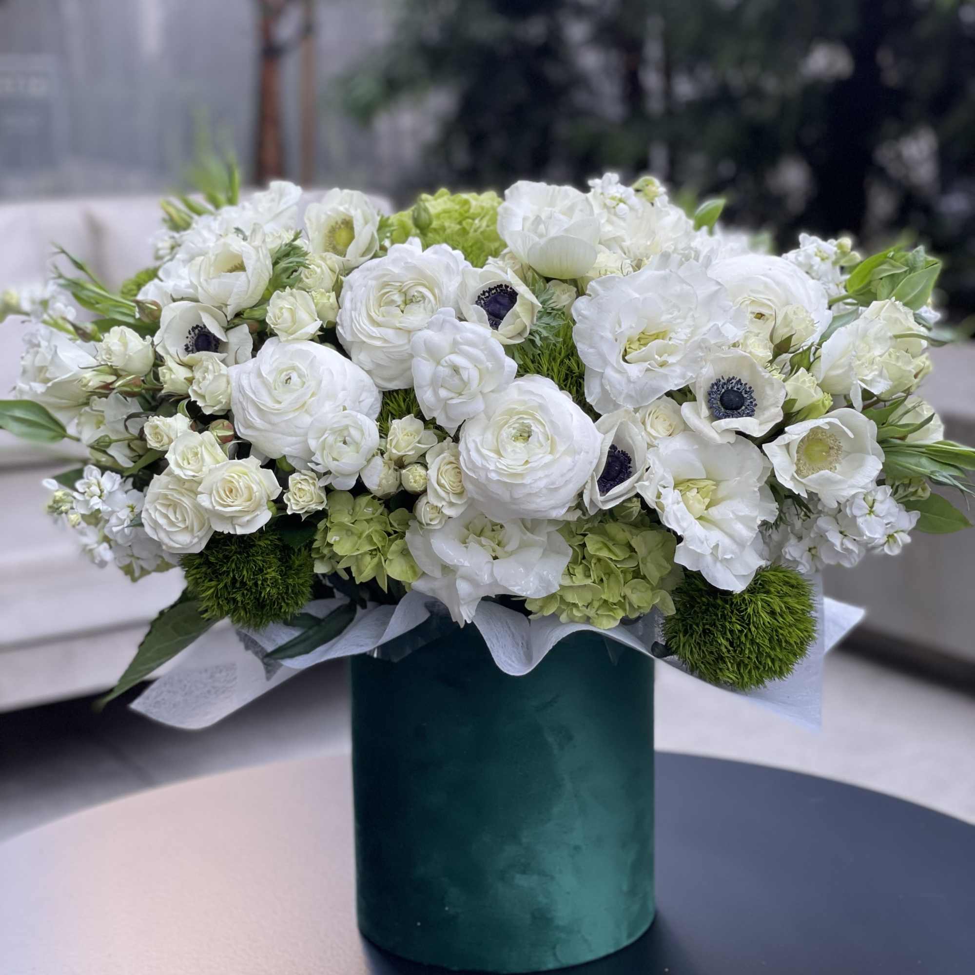 White floral arrangement in a teal vase with round blooms and green accents