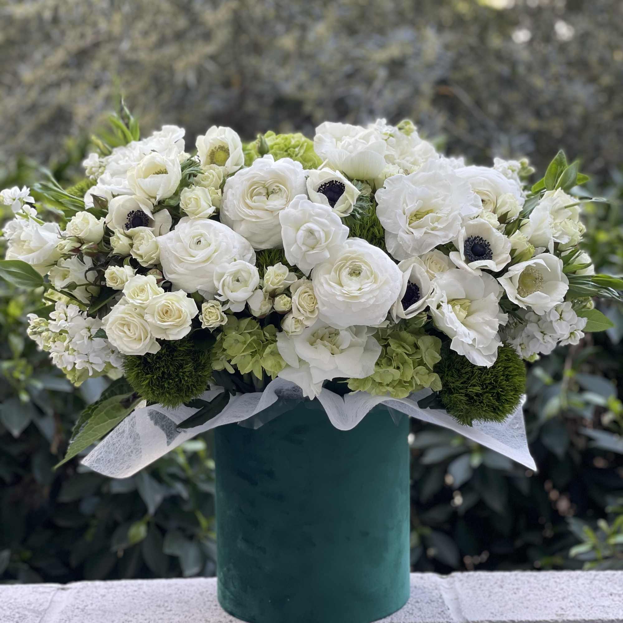 White floral arrangement in a teal vase with green accents