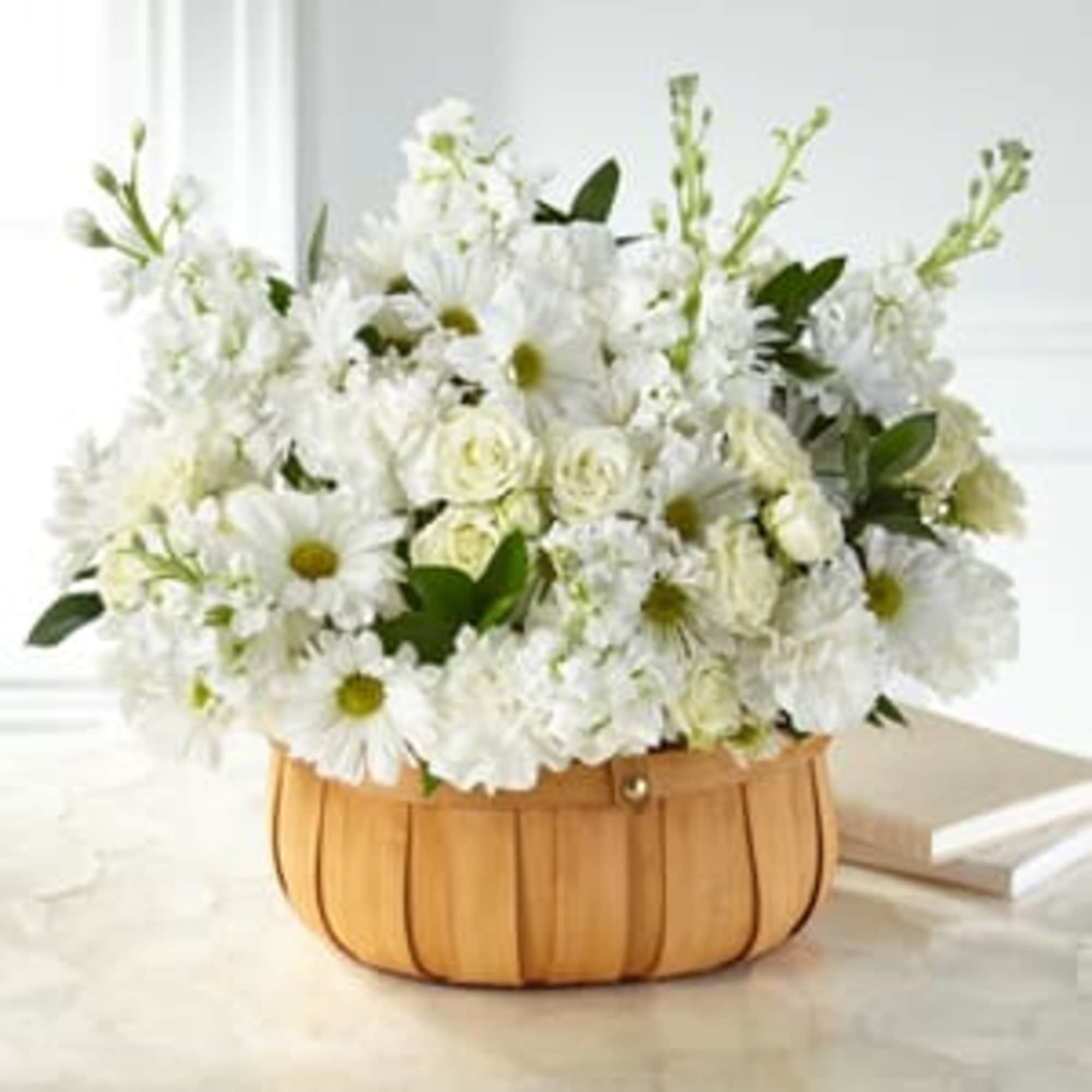 White floral arrangement in a tan basket with daisies and roses