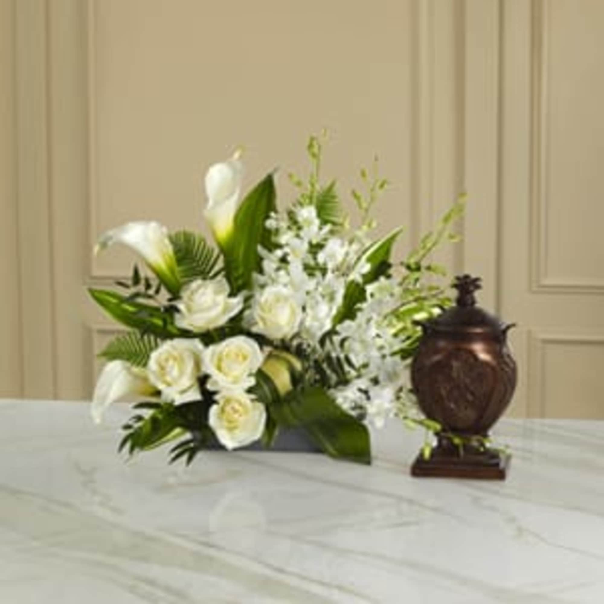 White floral arrangement with calla lilies and roses beside a dark urn