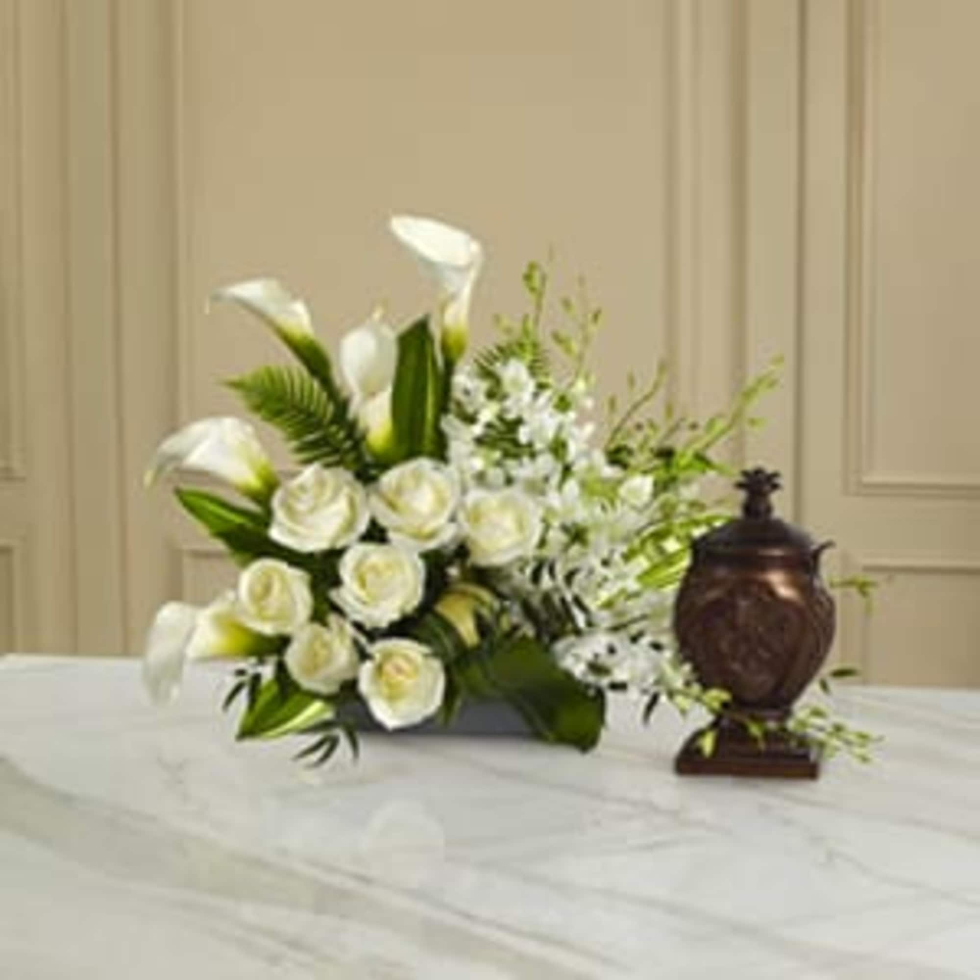 White calla lilies and roses arranged with greenery beside a dark urn
