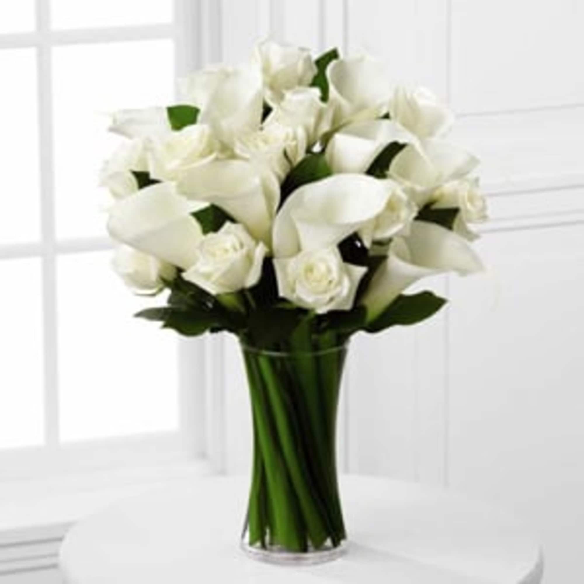 White calla lilies and roses arranged in a clear glass vase, photo 3 of 3