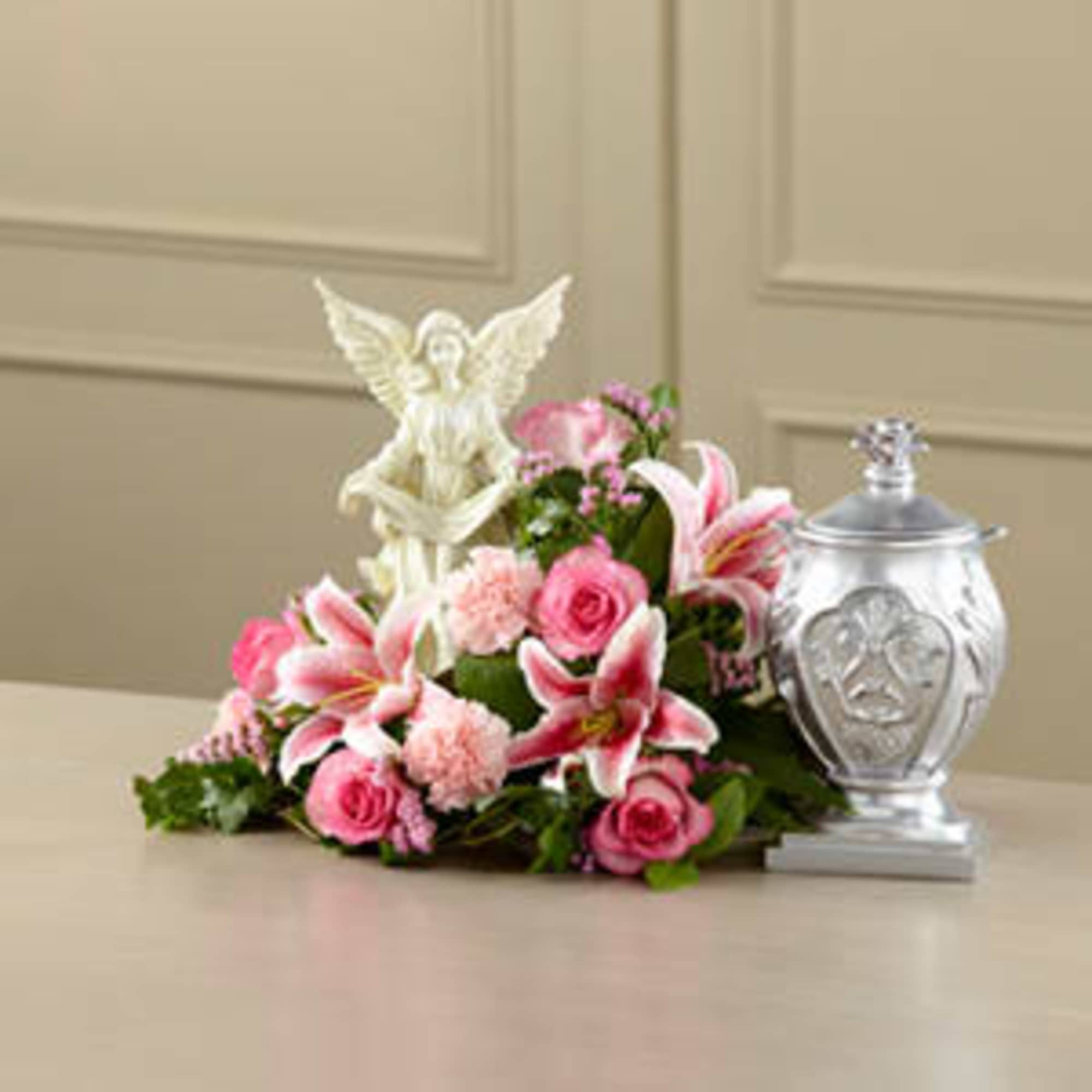 Pink floral arrangement with lilies and roses beside a silver urn and angel figurine