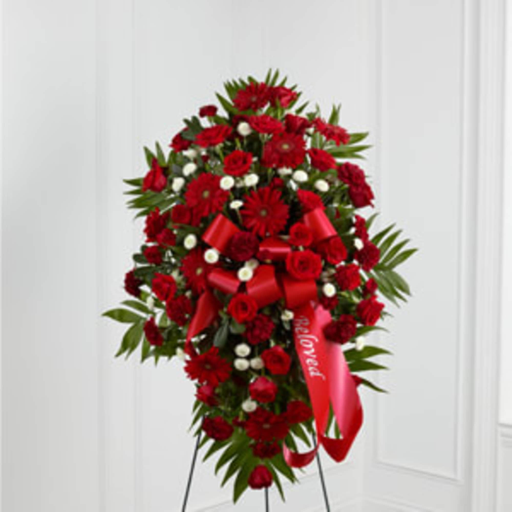 Standing spray of red flowers with a red ribbon on a metal easel