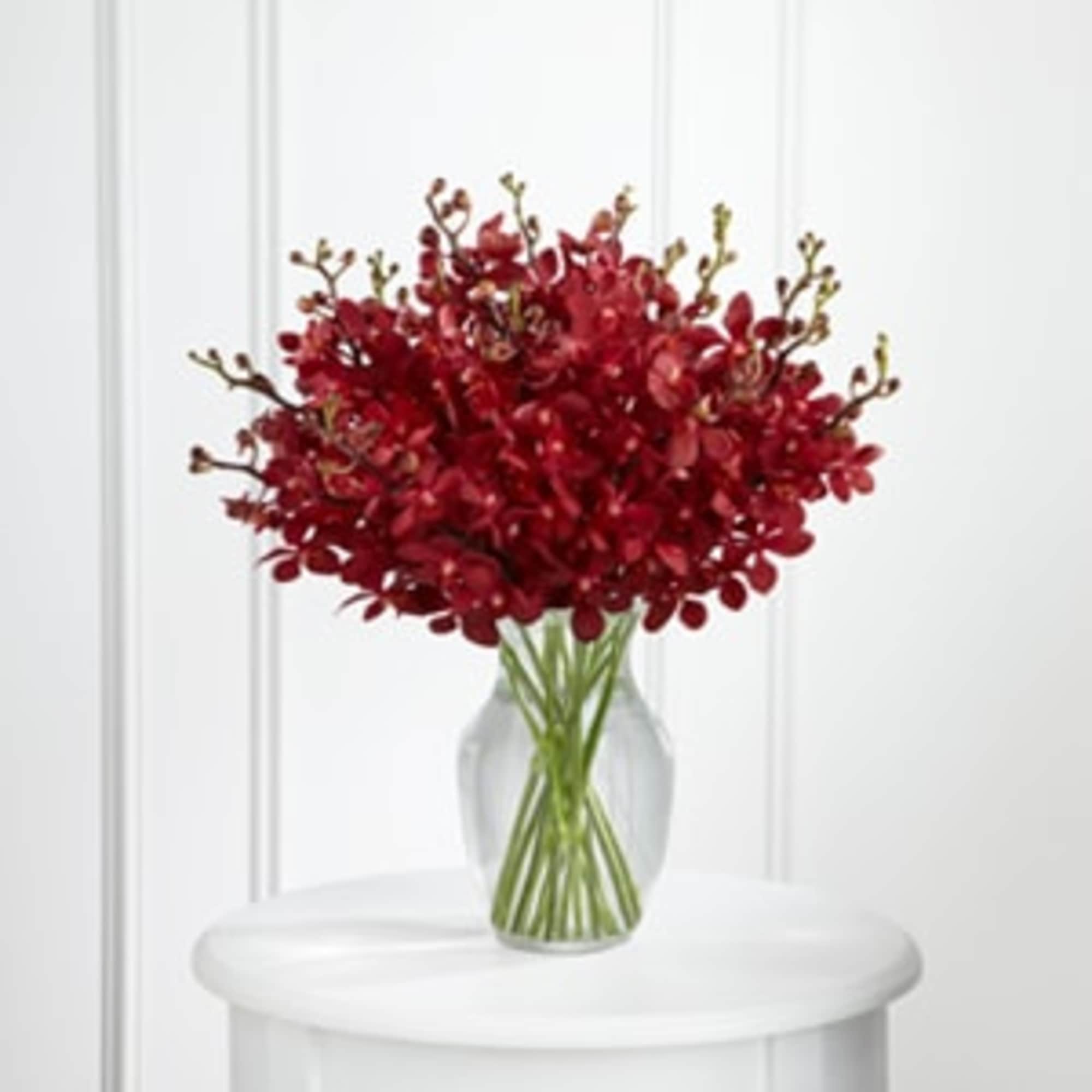 Red floral bouquet in a clear glass vase on a white table