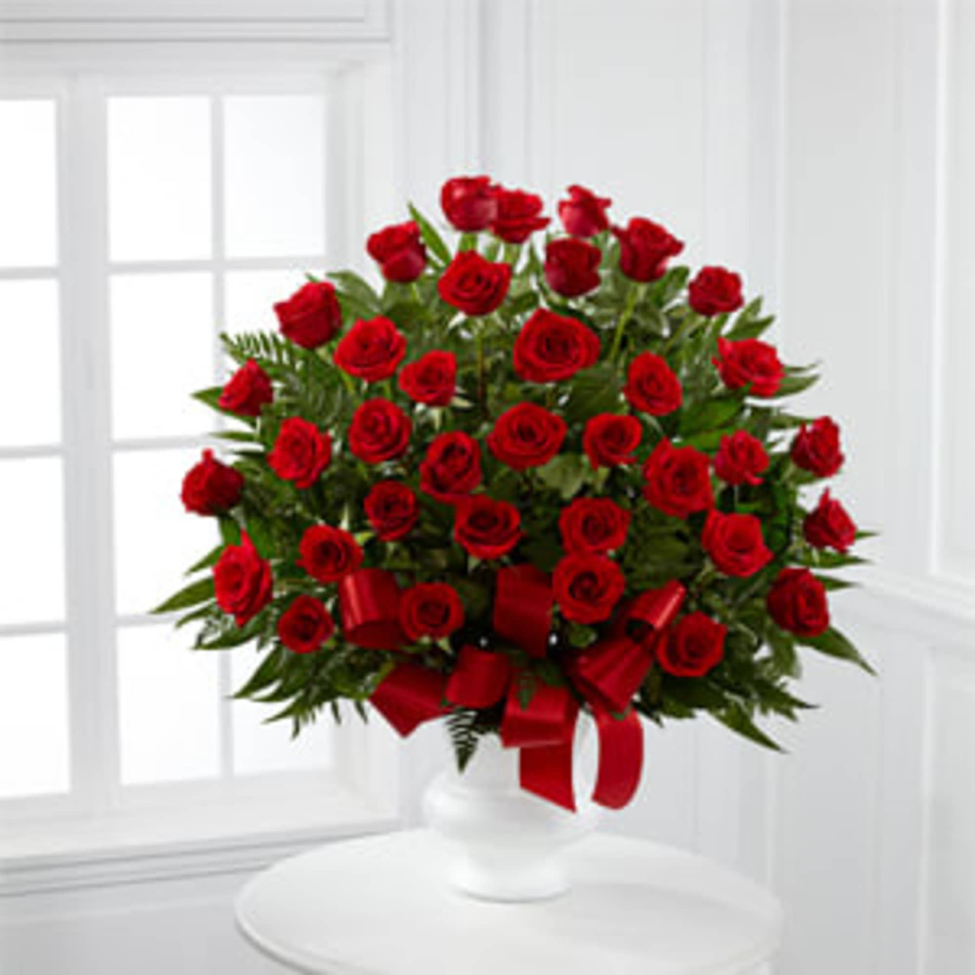 Red roses arranged in a white vase with a red ribbon