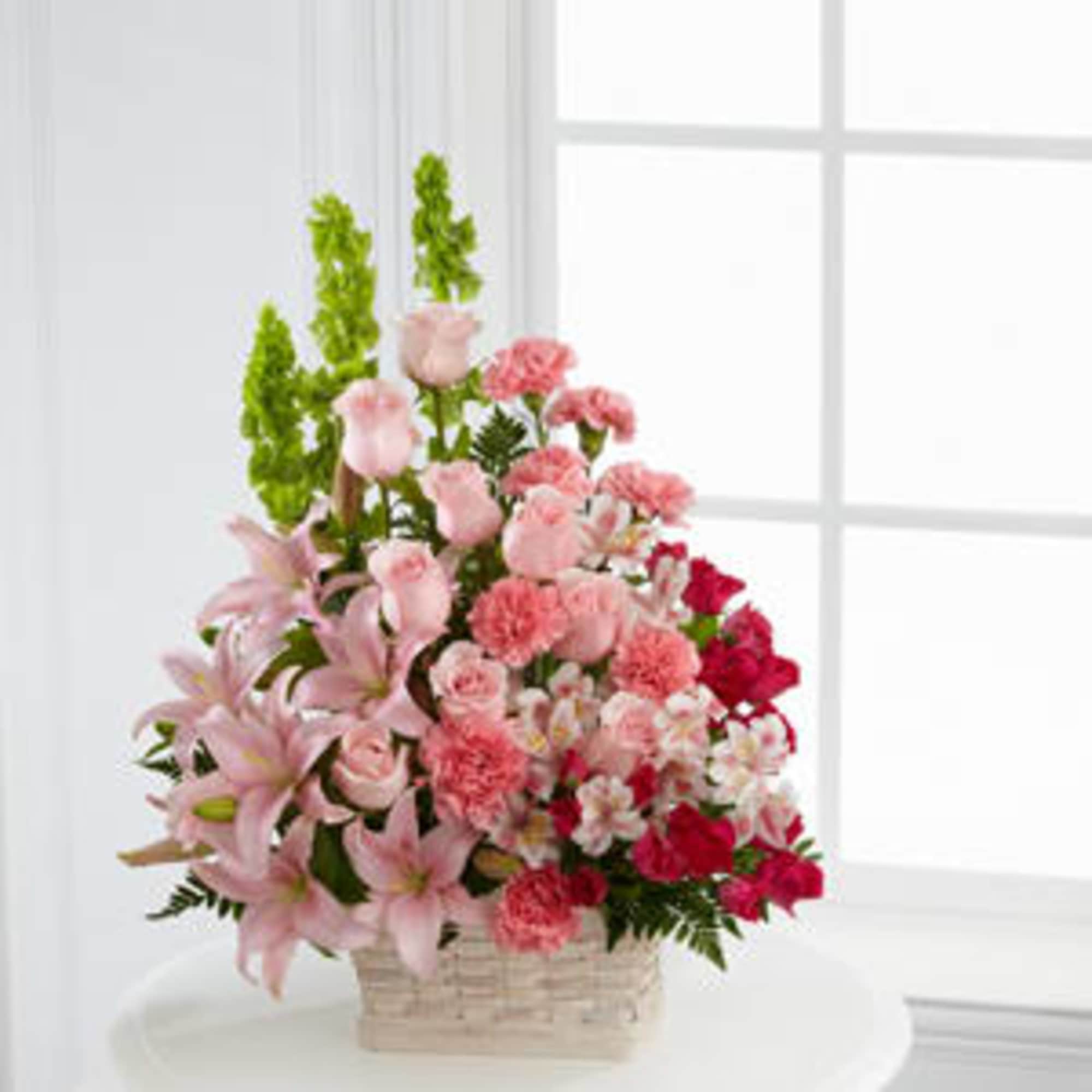 Pink lilies, carnations, and roses arranged in a basket.