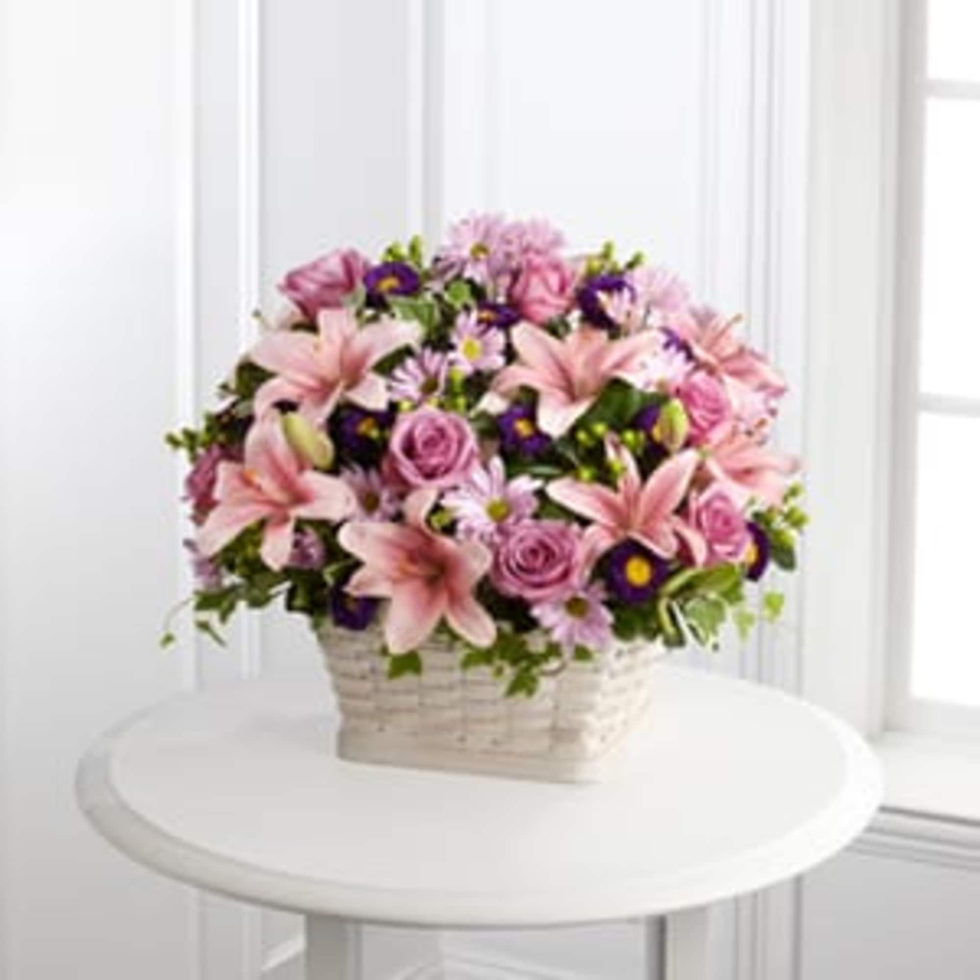 Pink lilies and roses in a white basket with purple accents