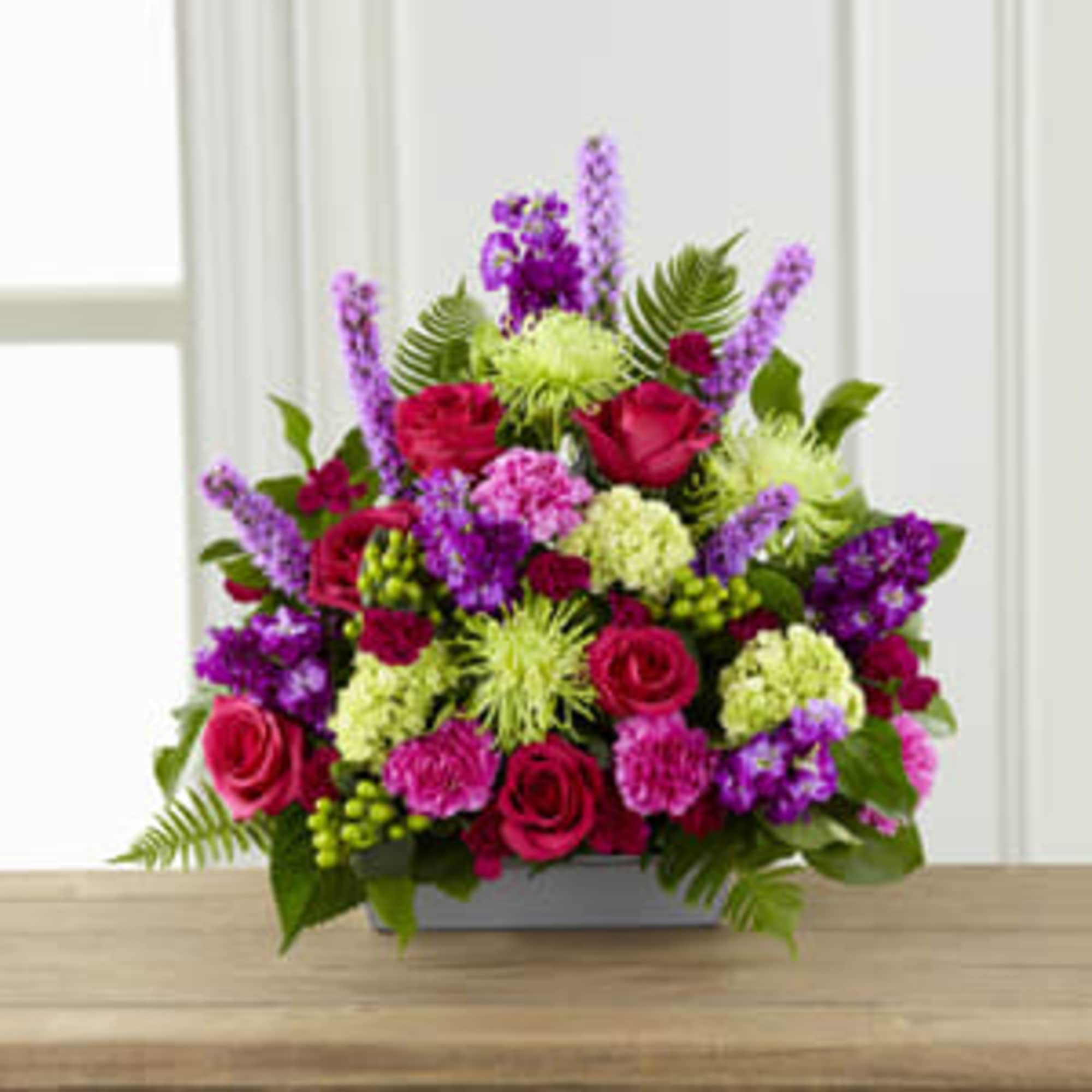 Mixed bouquet of pink, purple, and green flowers in a low rectangular container