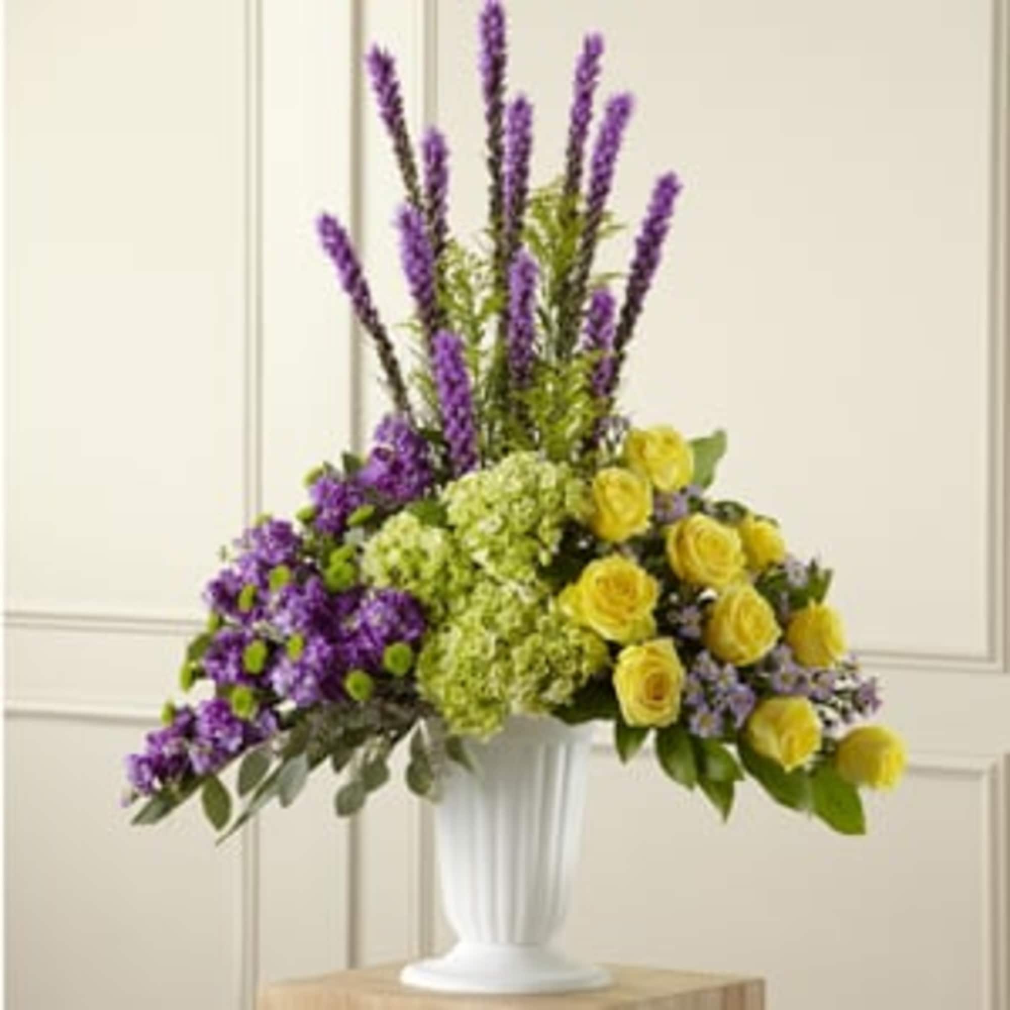 Purple and yellow floral arrangement in a white pedestal vase