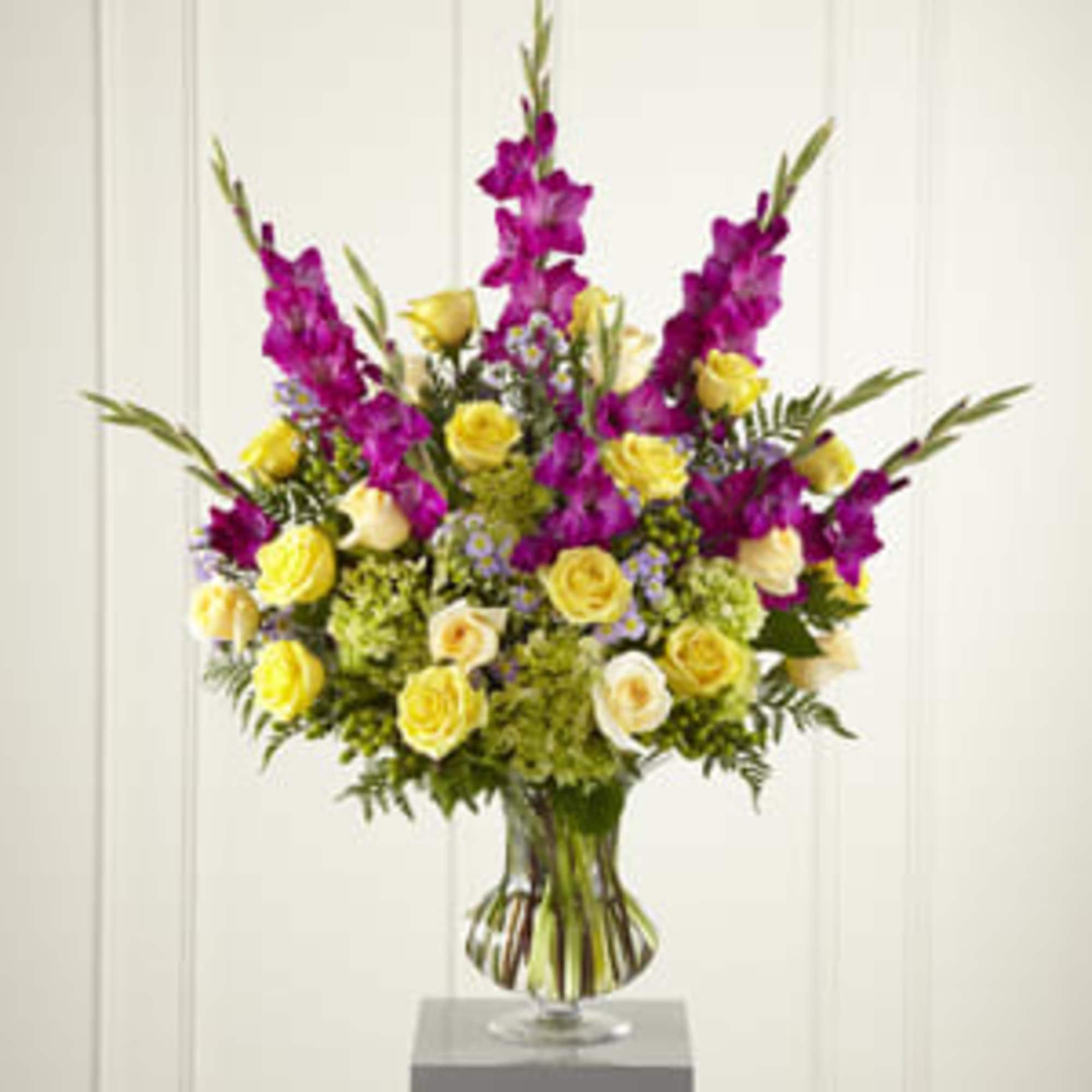 Tall bouquet of yellow roses and purple flowers in a glass vase