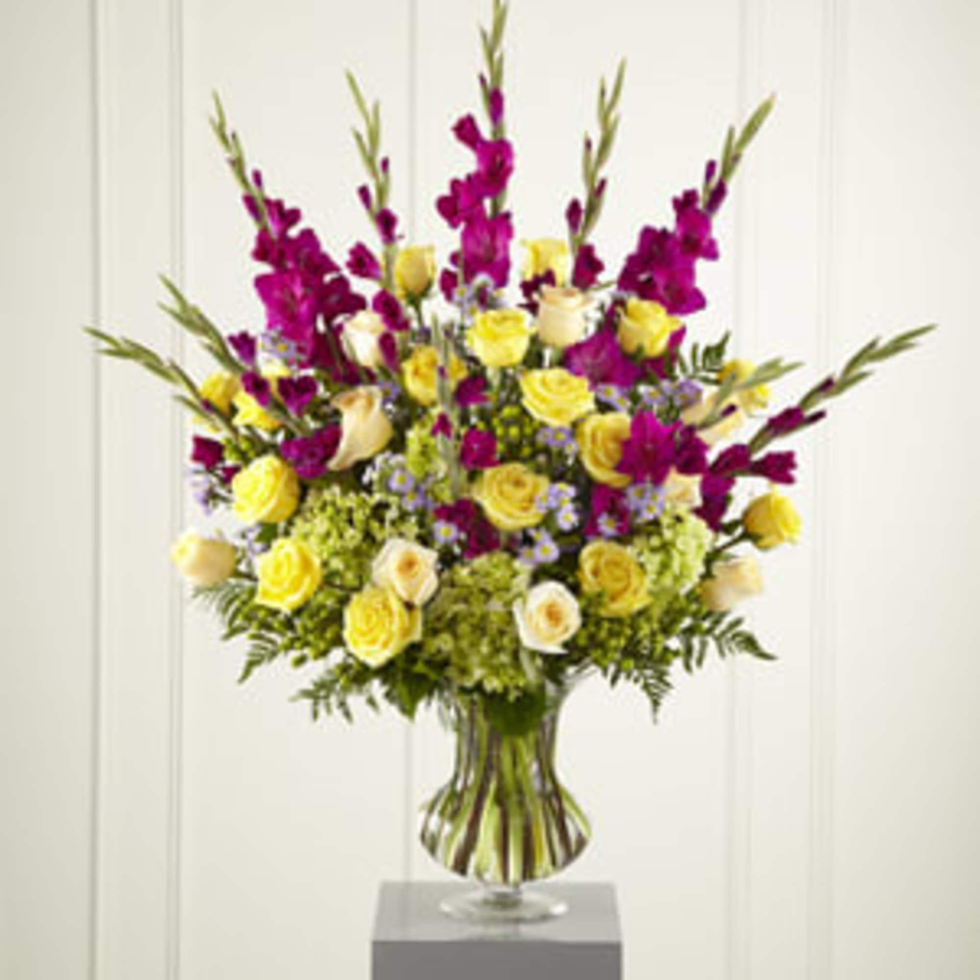 Tall bouquet of yellow and cream roses with purple flowers in a glass vase