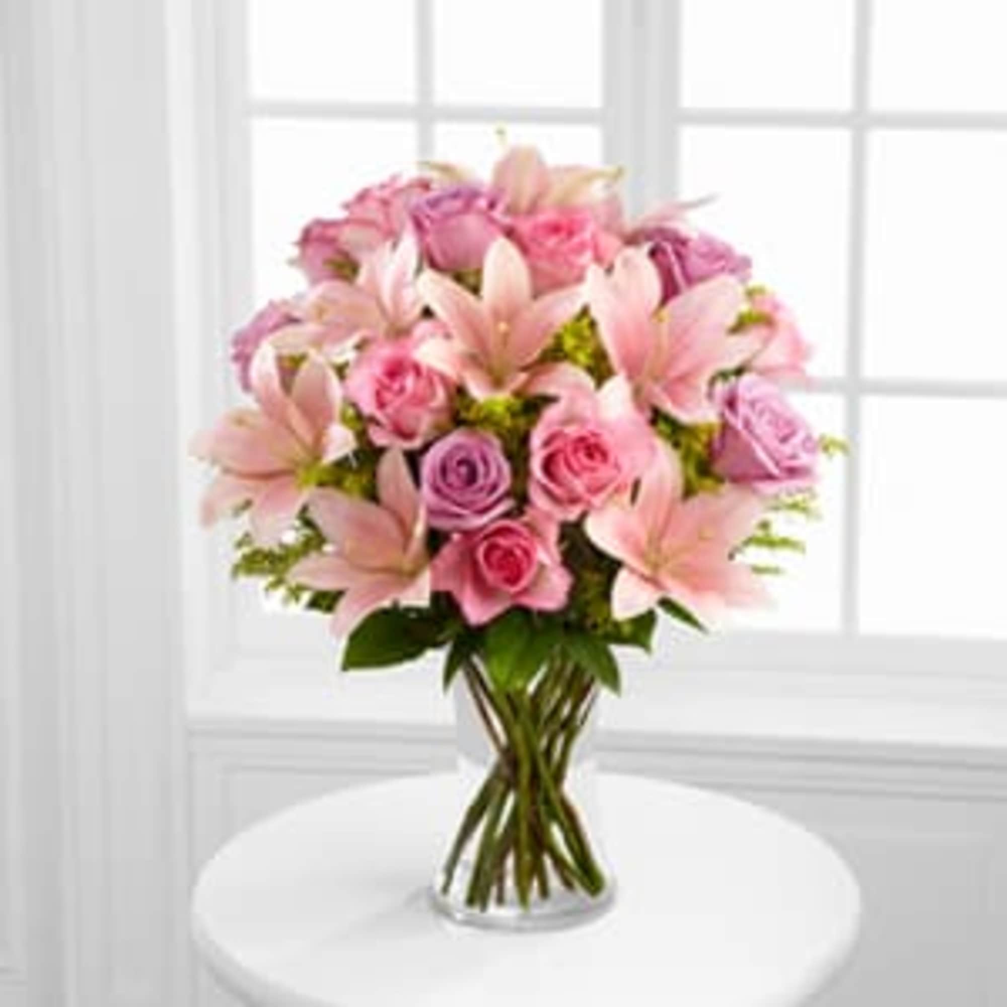 Pink lilies and roses arranged in a clear glass vase