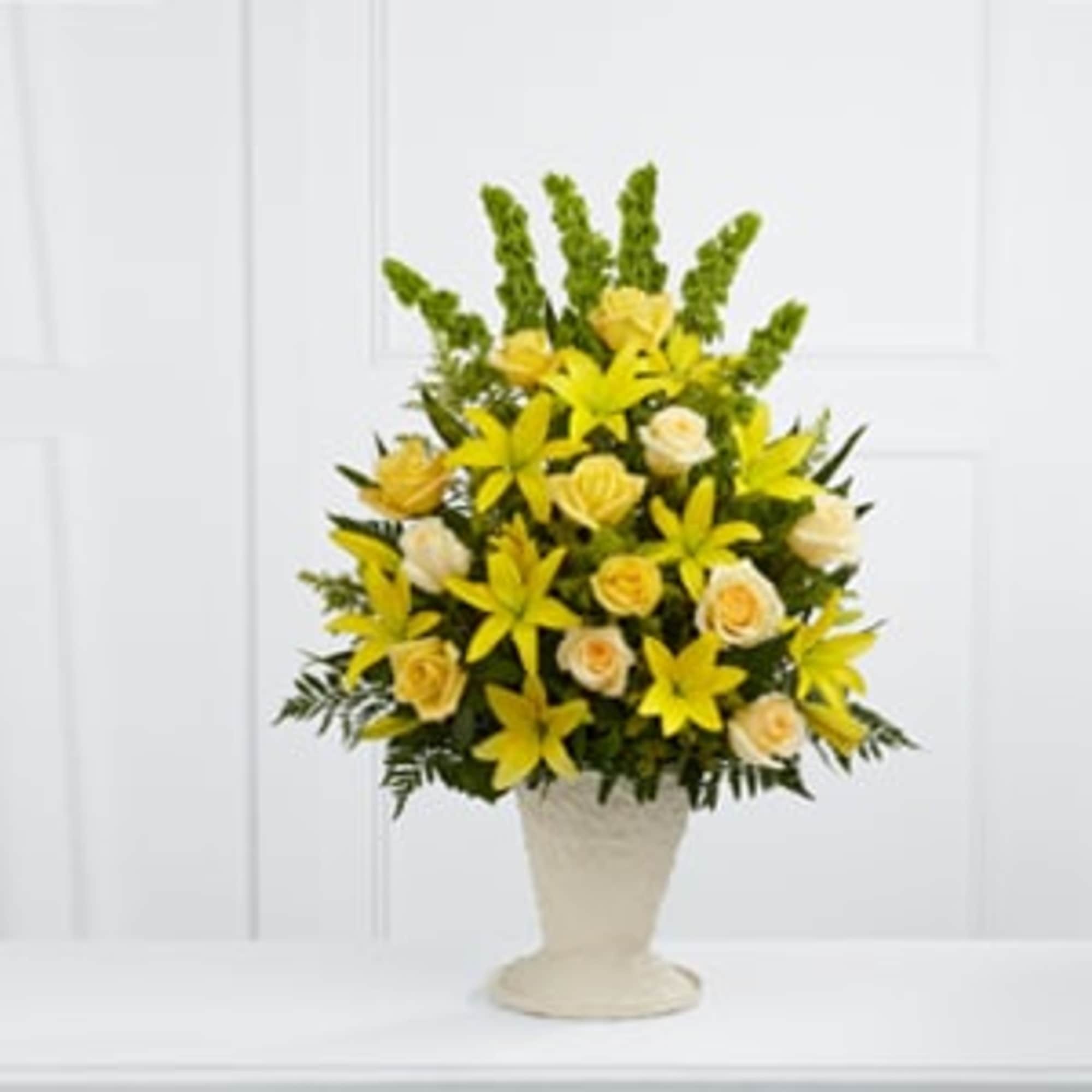 Yellow lilies and cream roses arranged in a white vase