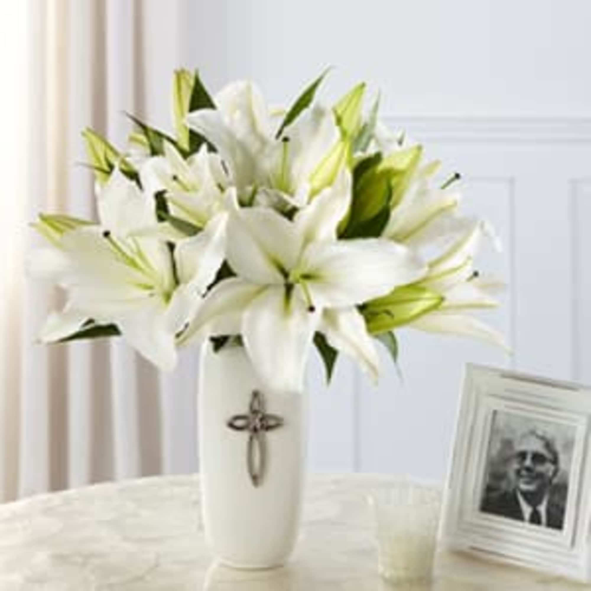 White lilies in a tall white vase with a cross emblem