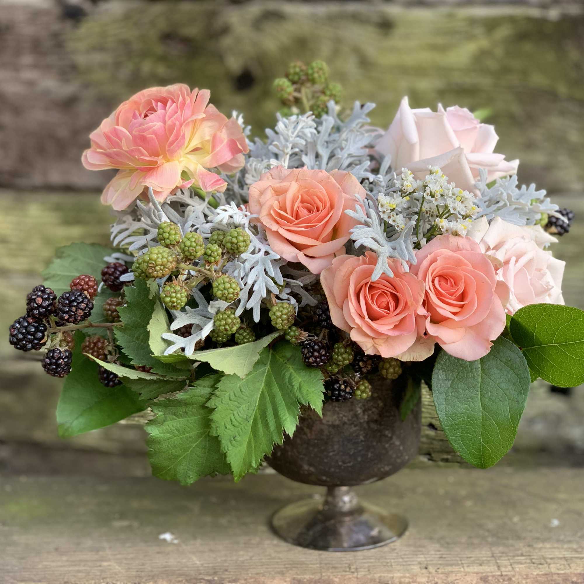 Peach roses and pink blooms in a metal pedestal vase