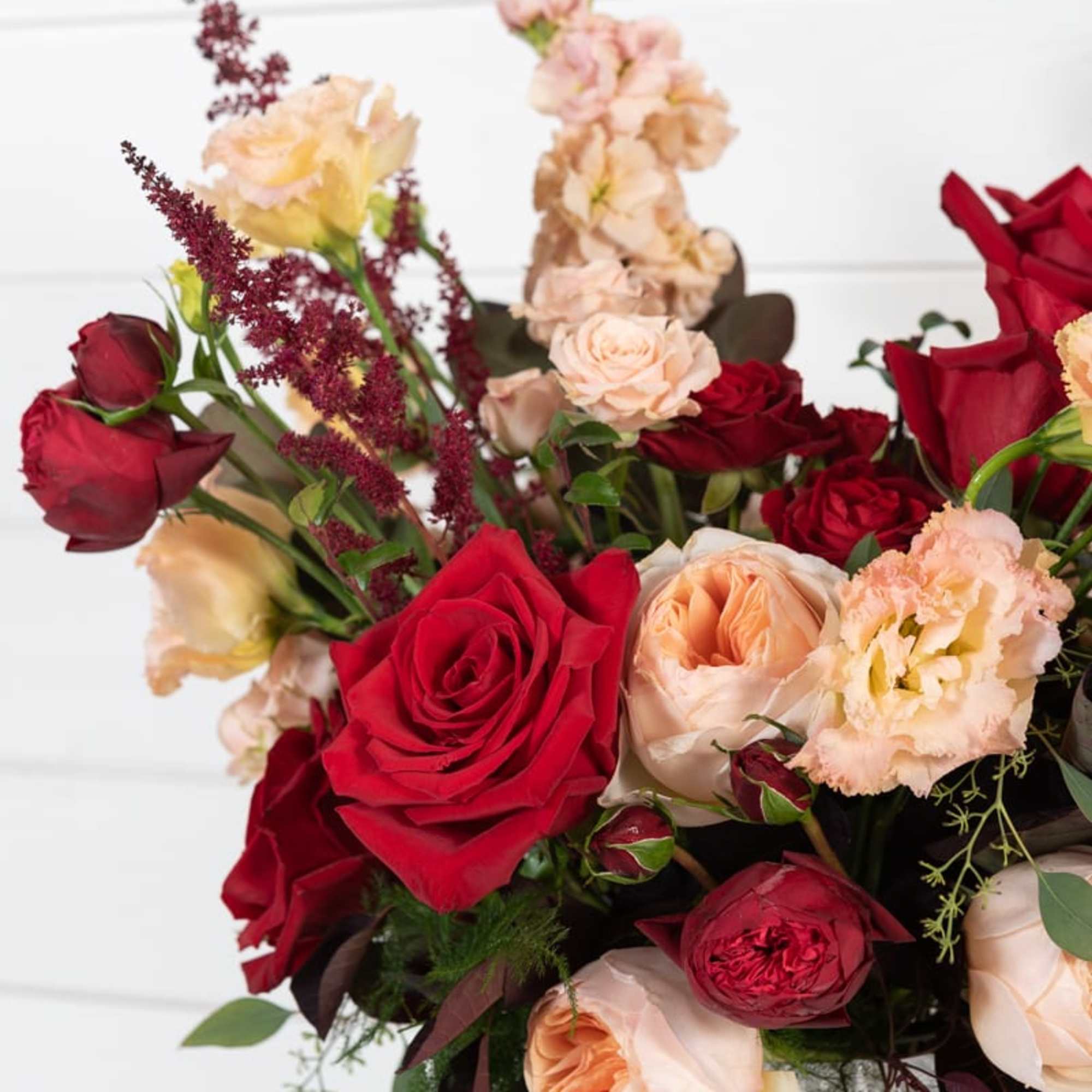 Bouquet of red and blush roses with peach flowers in a glass vase