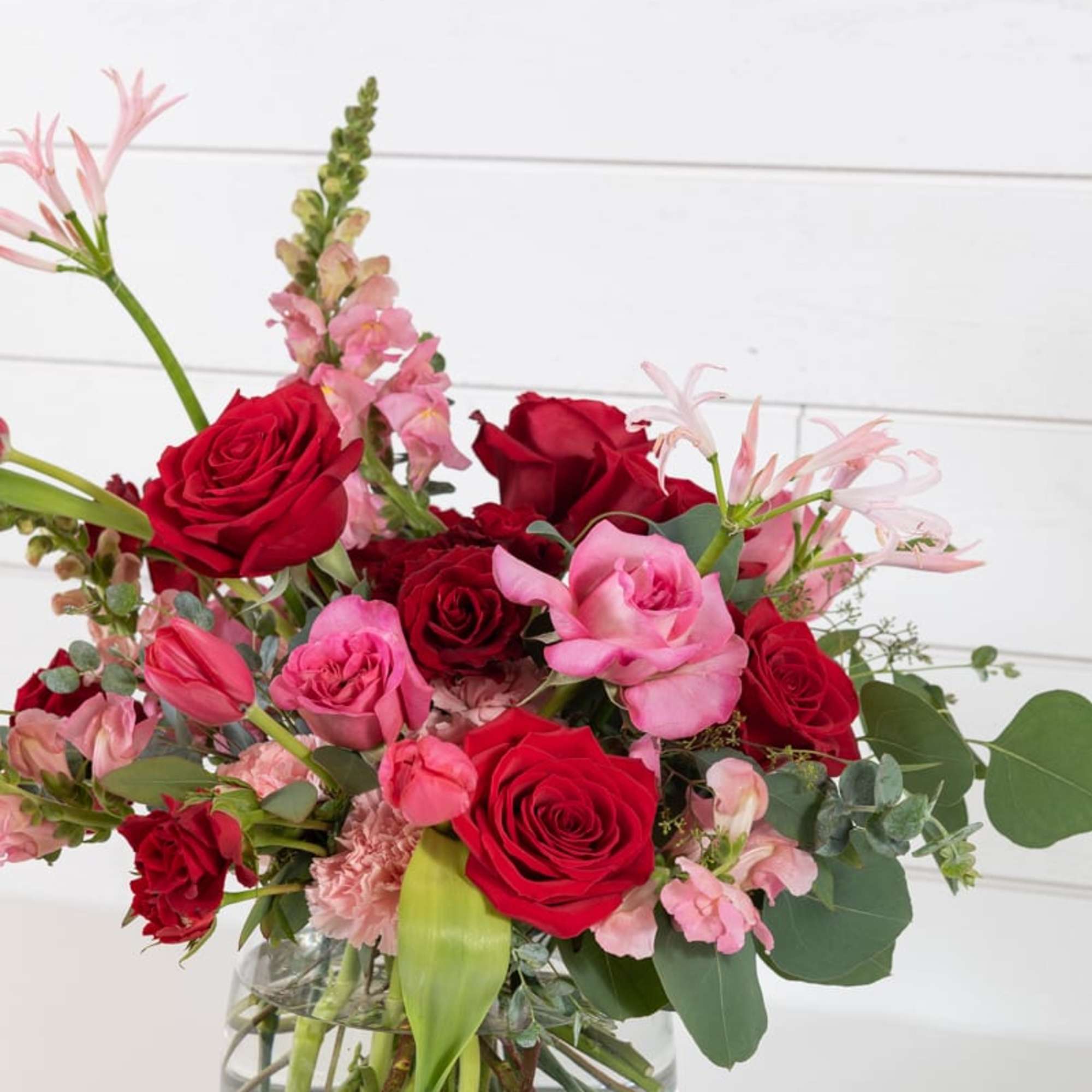 Red and pink roses in a clear glass vase with greenery