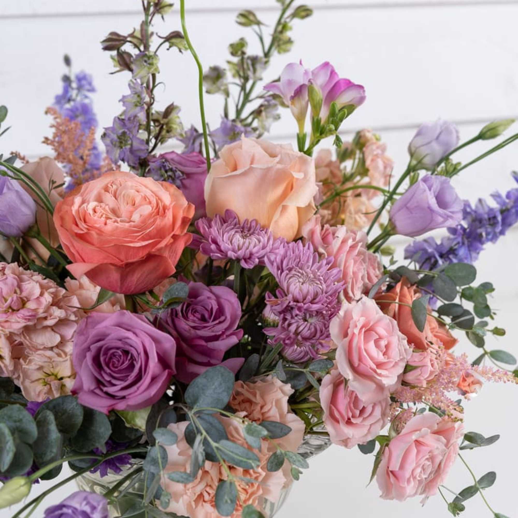 Mixed bouquet of pink, purple, and peach flowers in a clear glass vase