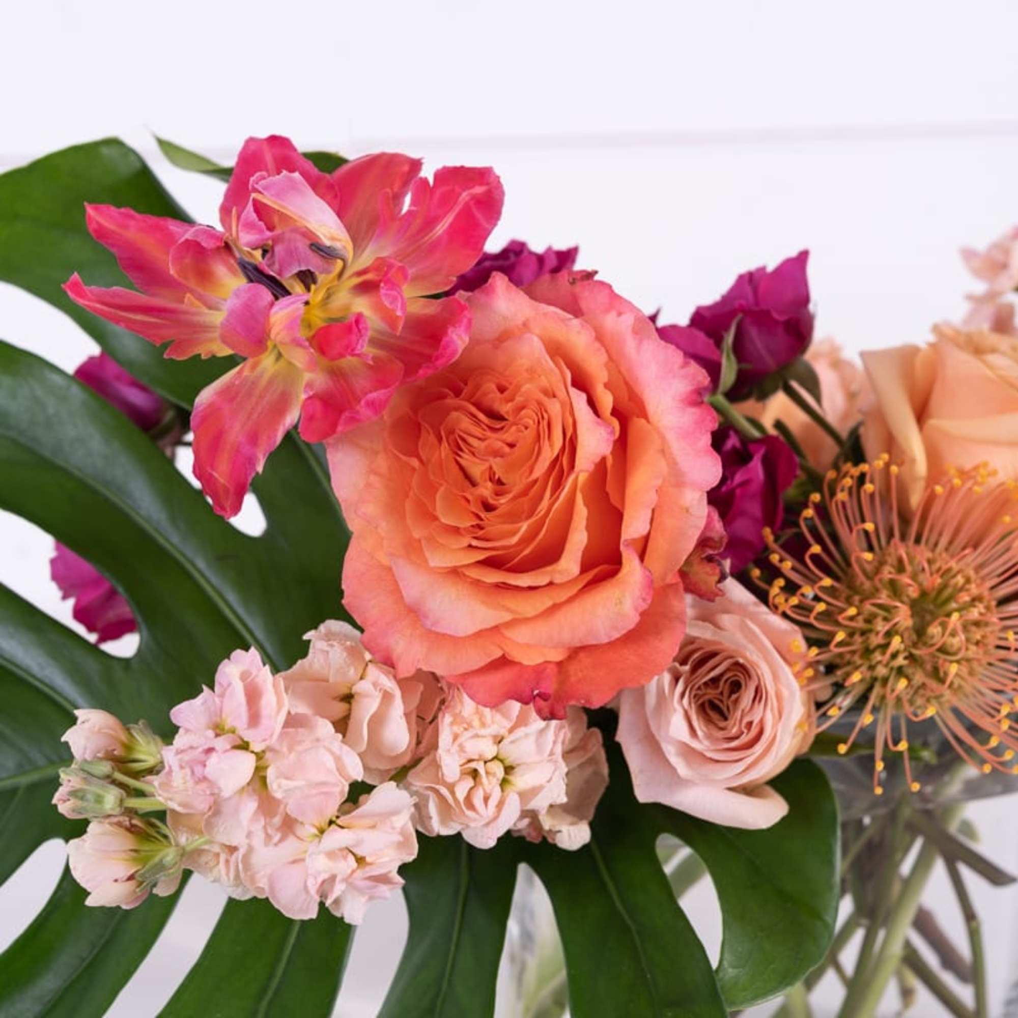 Bouquet of peach and pink roses with tropical flowers in a glass vase