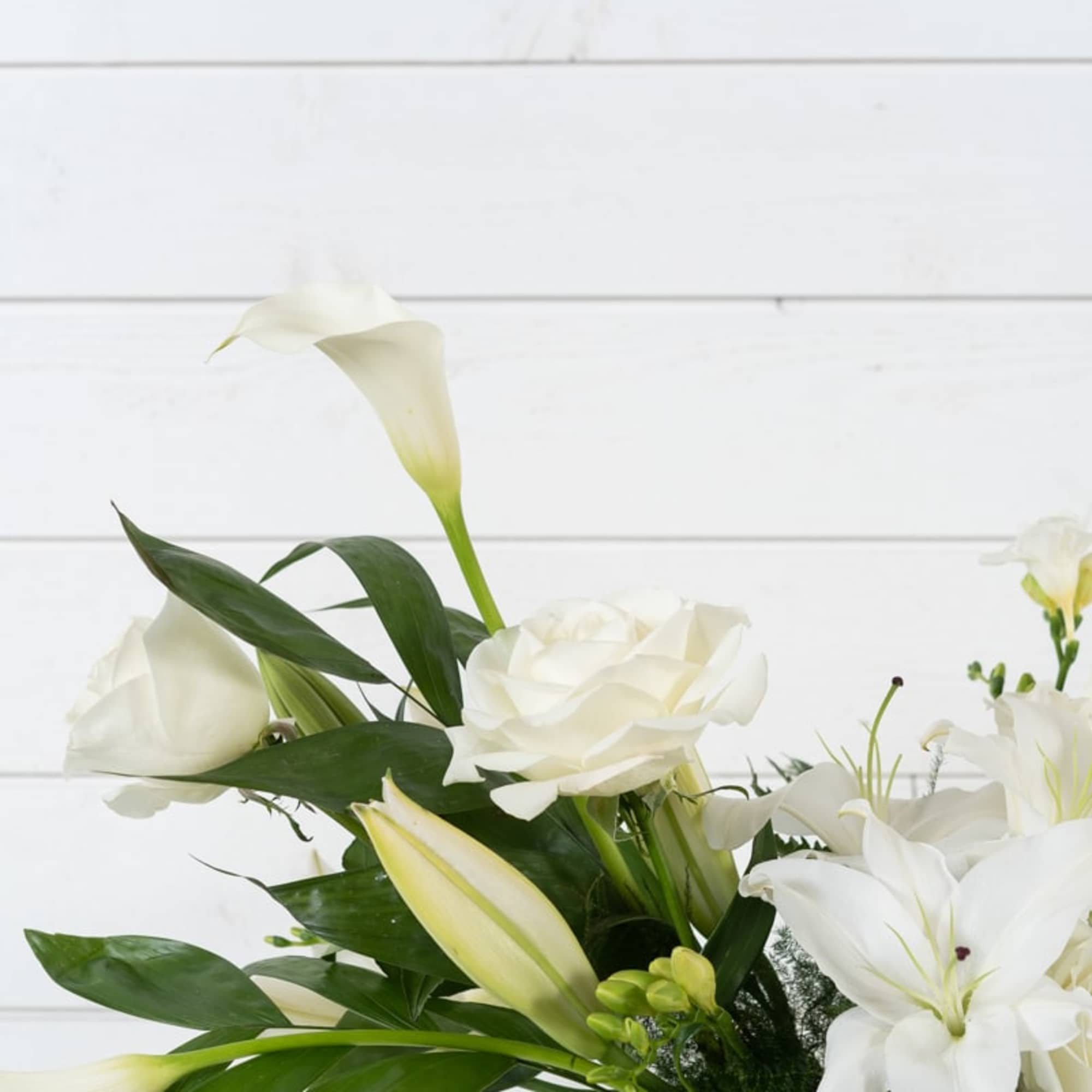 White calla lilies and lilies arranged in a clear glass vase