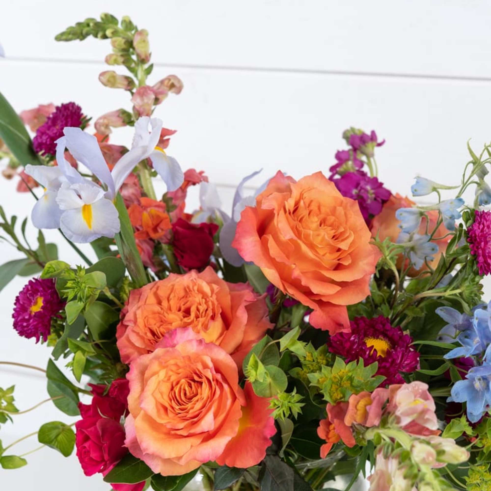 Colorful bouquet of orange roses and mixed blooms in a glass vase