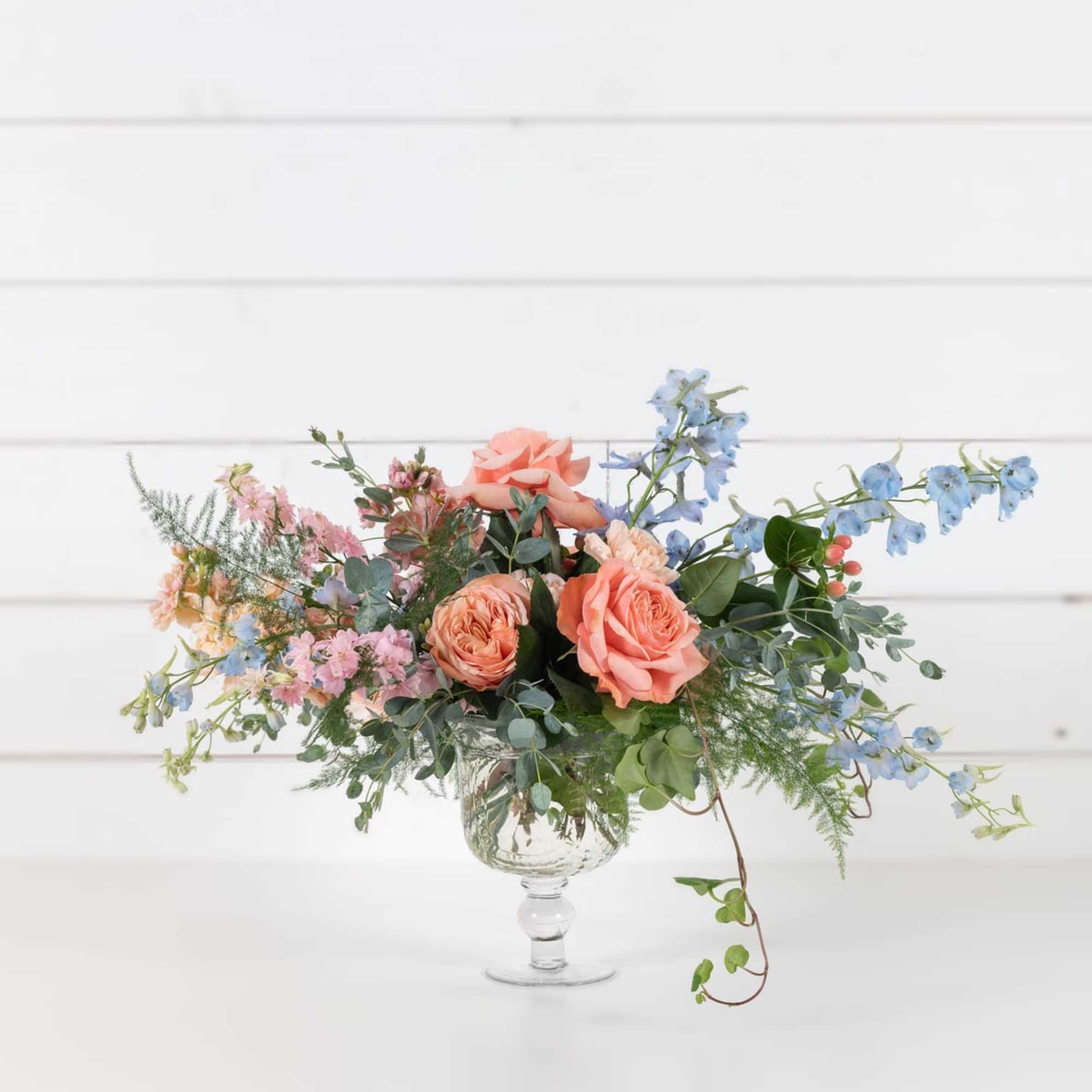Peach roses and blue flowers in a clear glass vase, photo 2 of 5