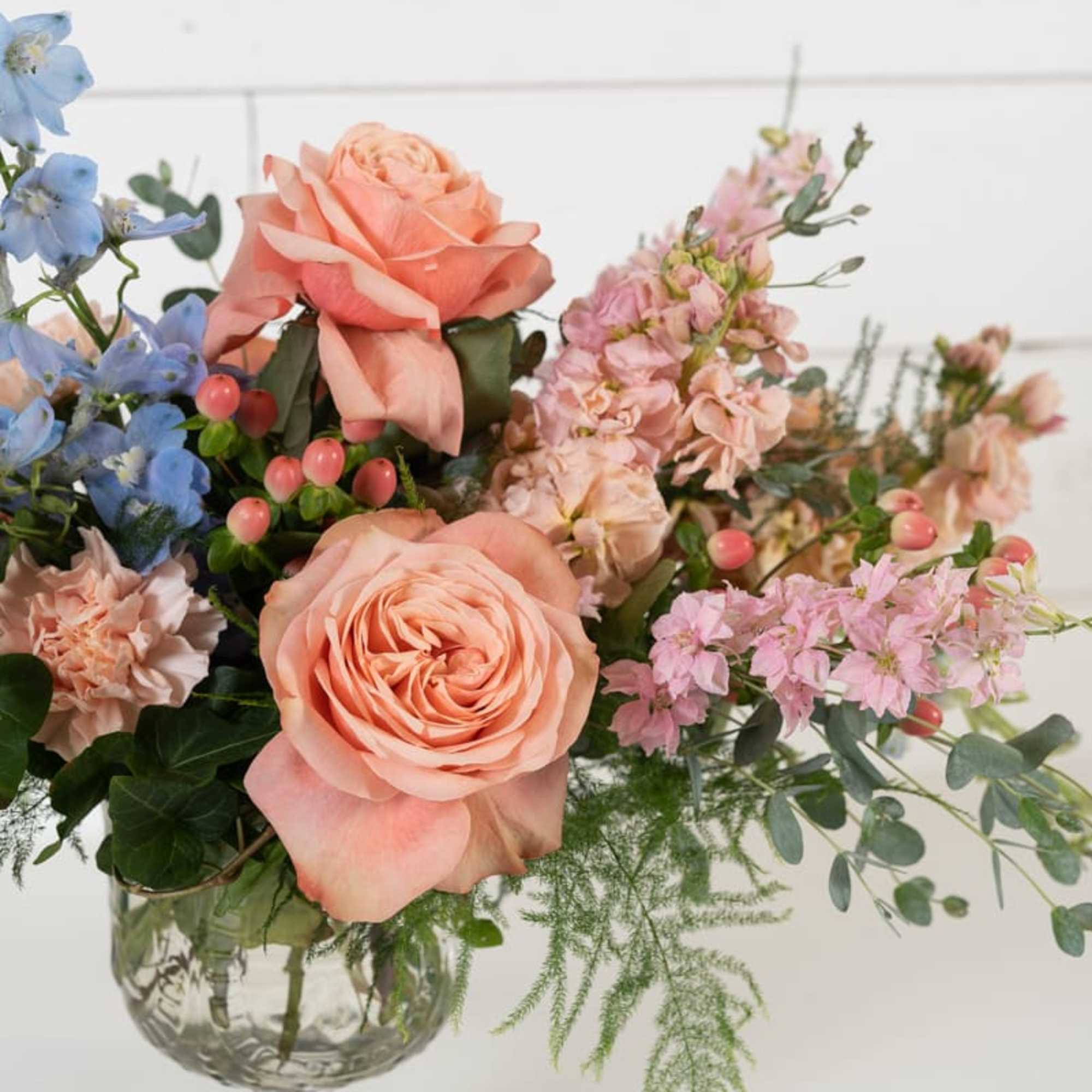 Peach and pink roses in a clear glass vase with blue and pink flowers