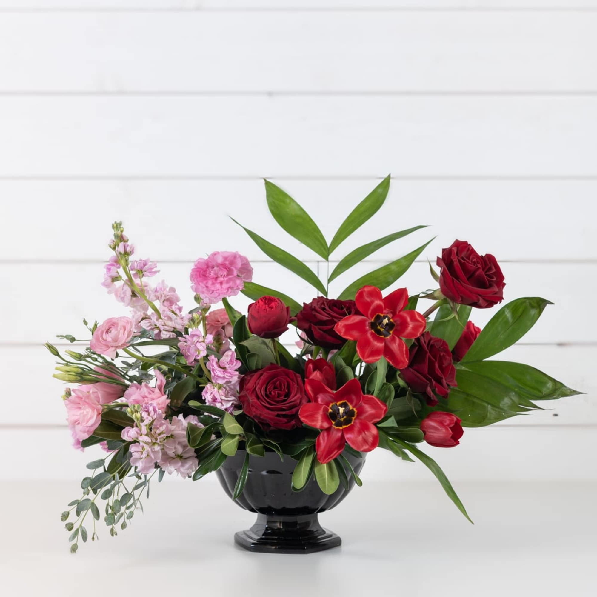 Red and pink floral arrangement in a black pedestal vase