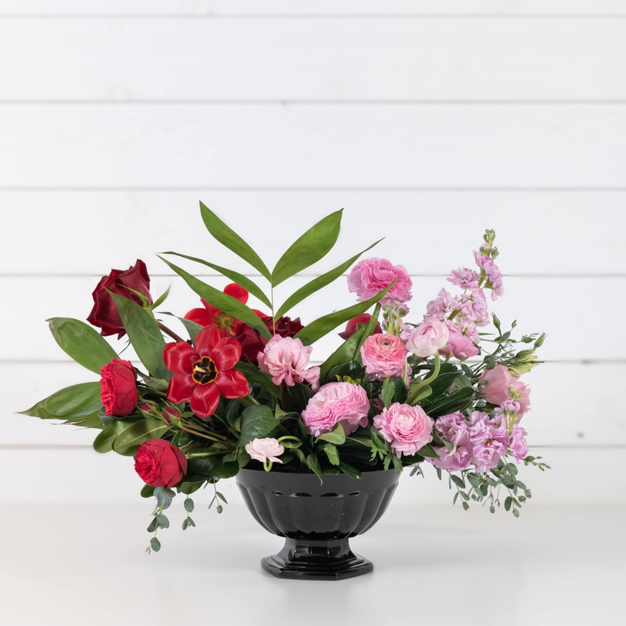 Red and pink floral arrangement in a black pedestal vase, photo 2 of 4