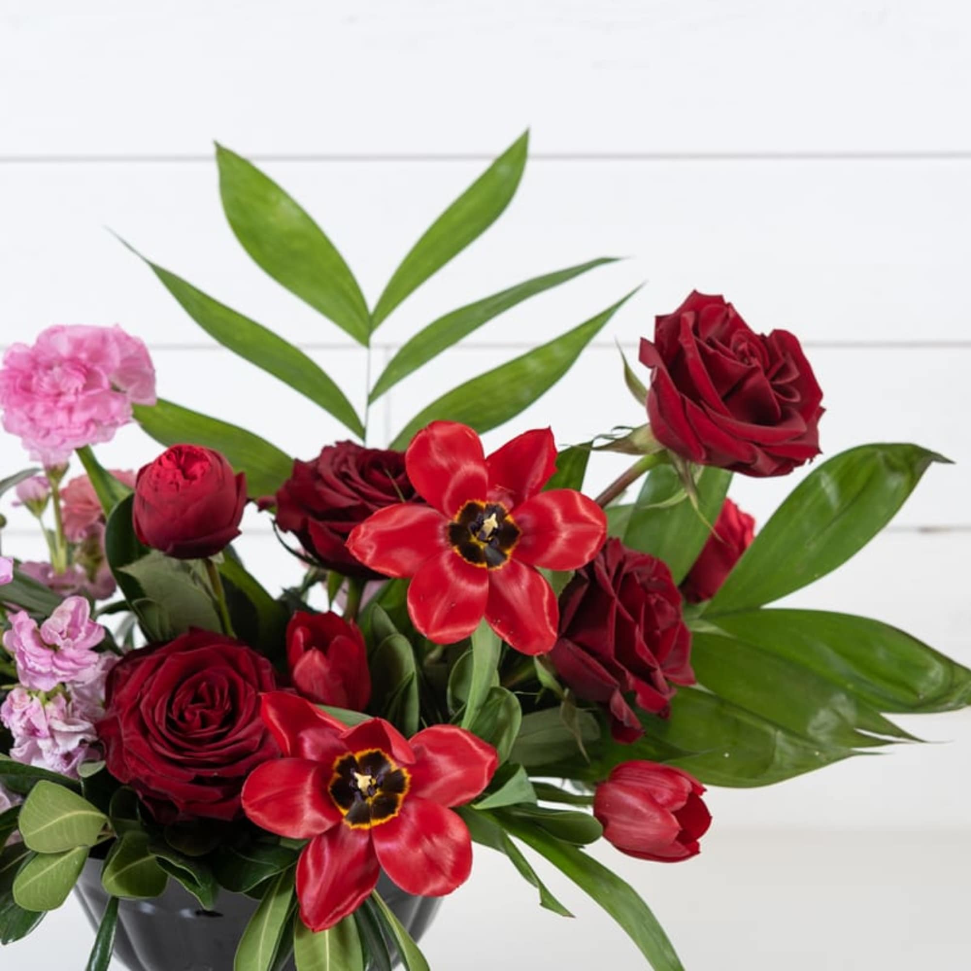 Red roses and tulips in a black vase with pink accent flowers