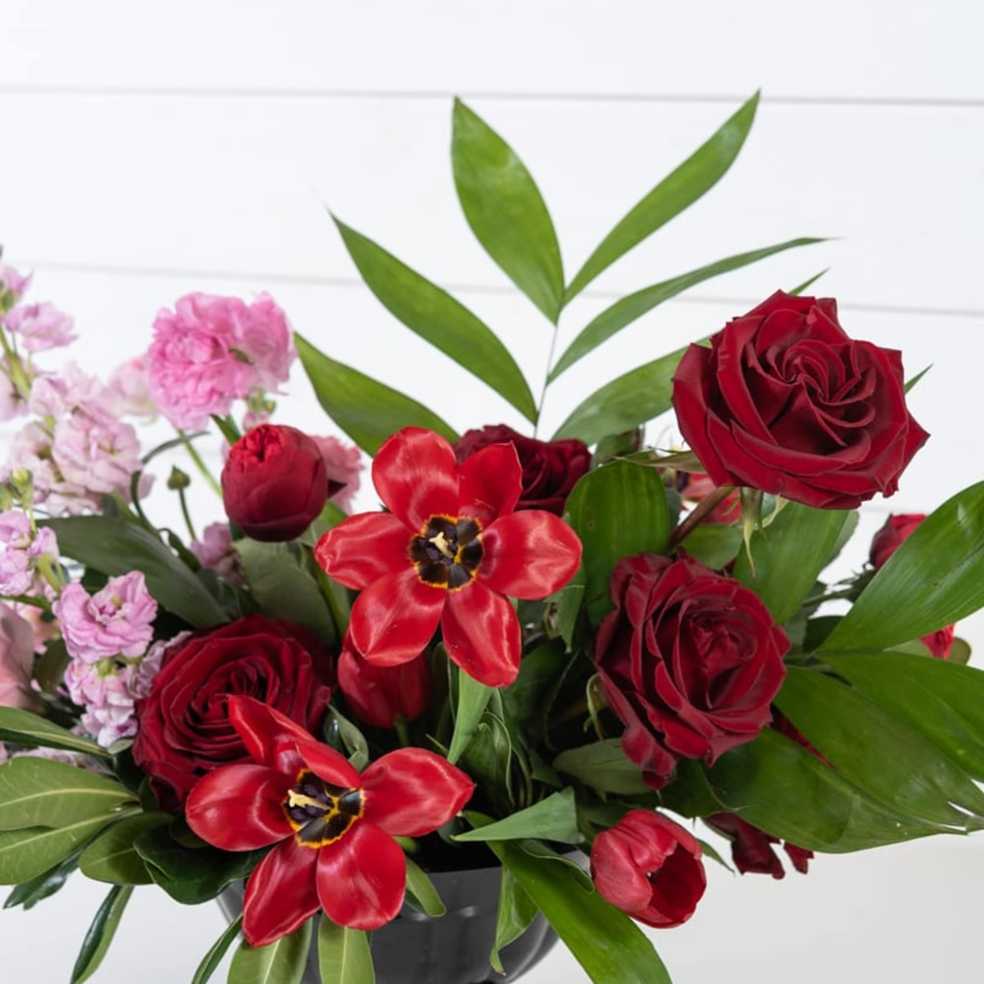 Red roses and red tulips in a black vase with pink flowers