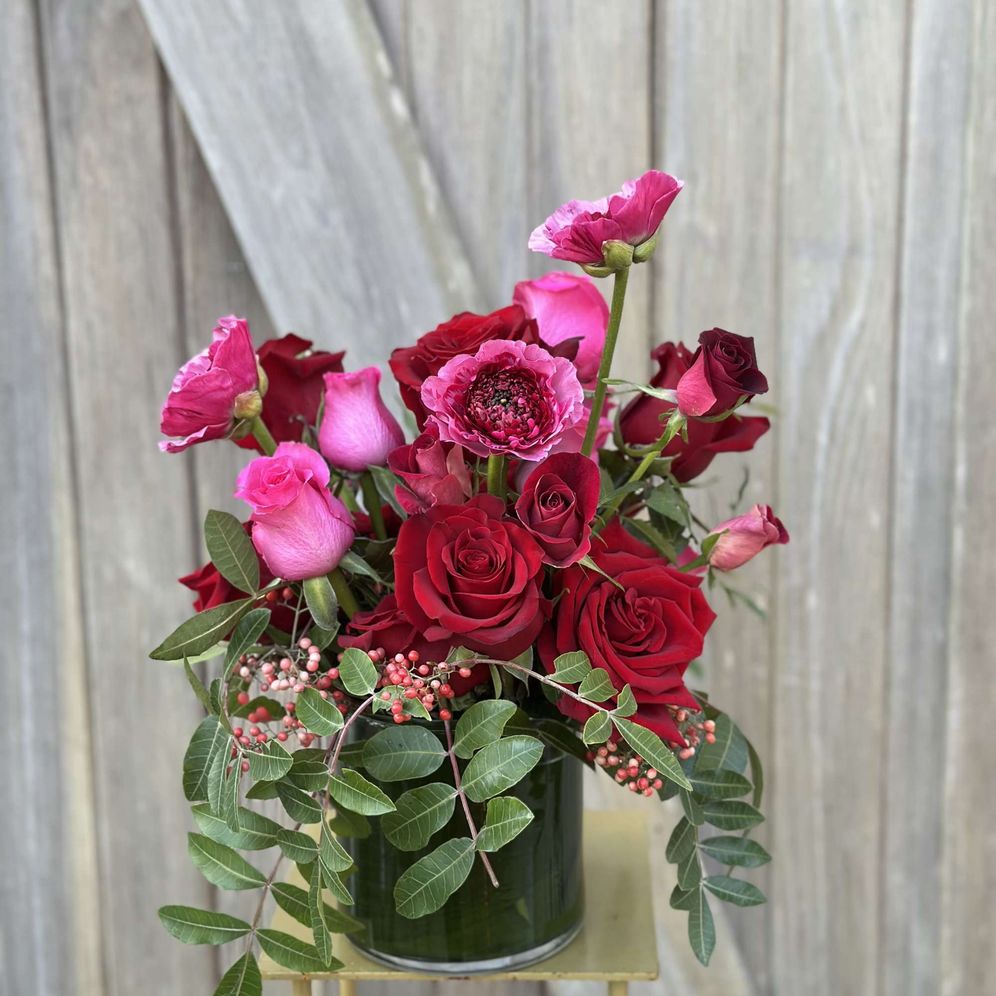 Red and pink roses arranged in a glass vase with trailing greenery.
