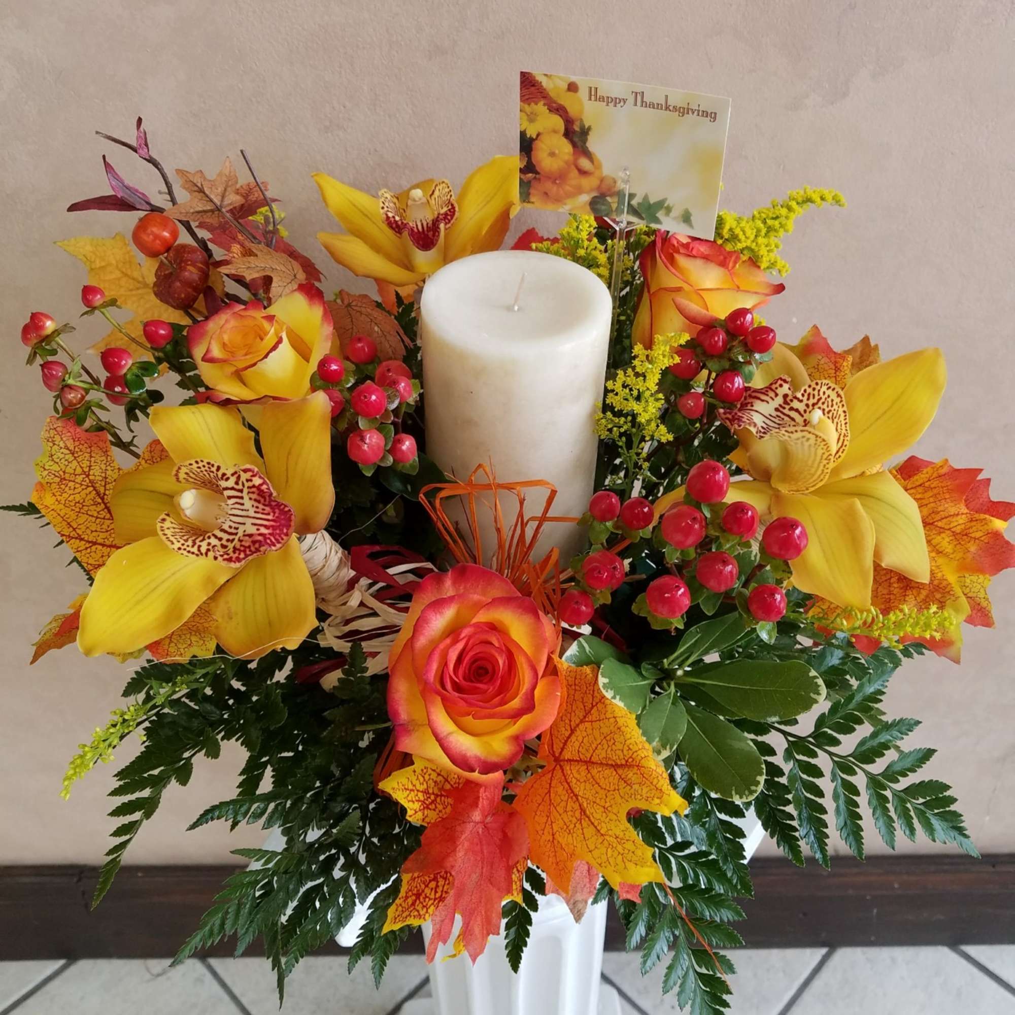 Yellow orchids and roses arranged around a white pillar candle in a vase