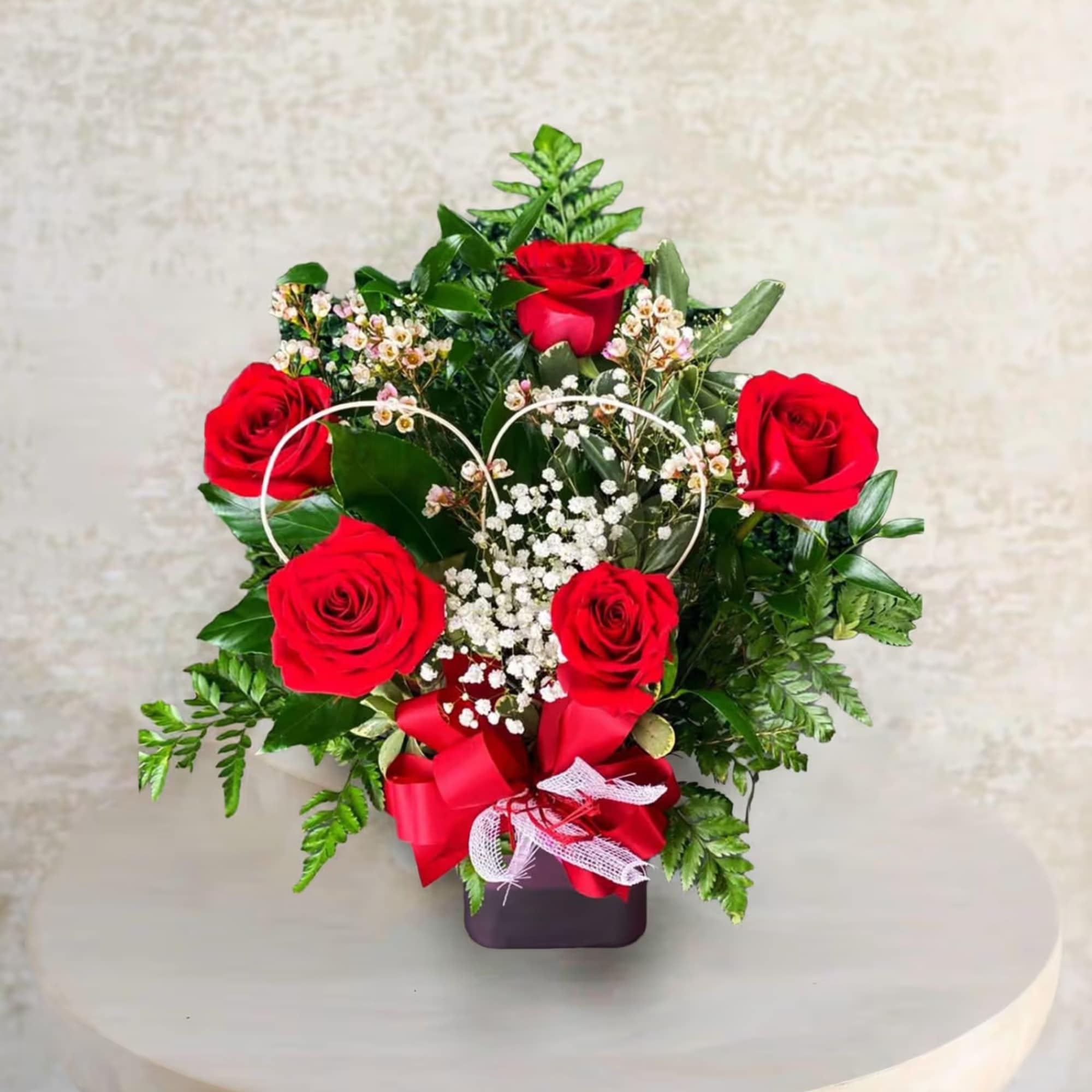 Red roses arranged in a heart-shaped design with baby's breath in a dark vase