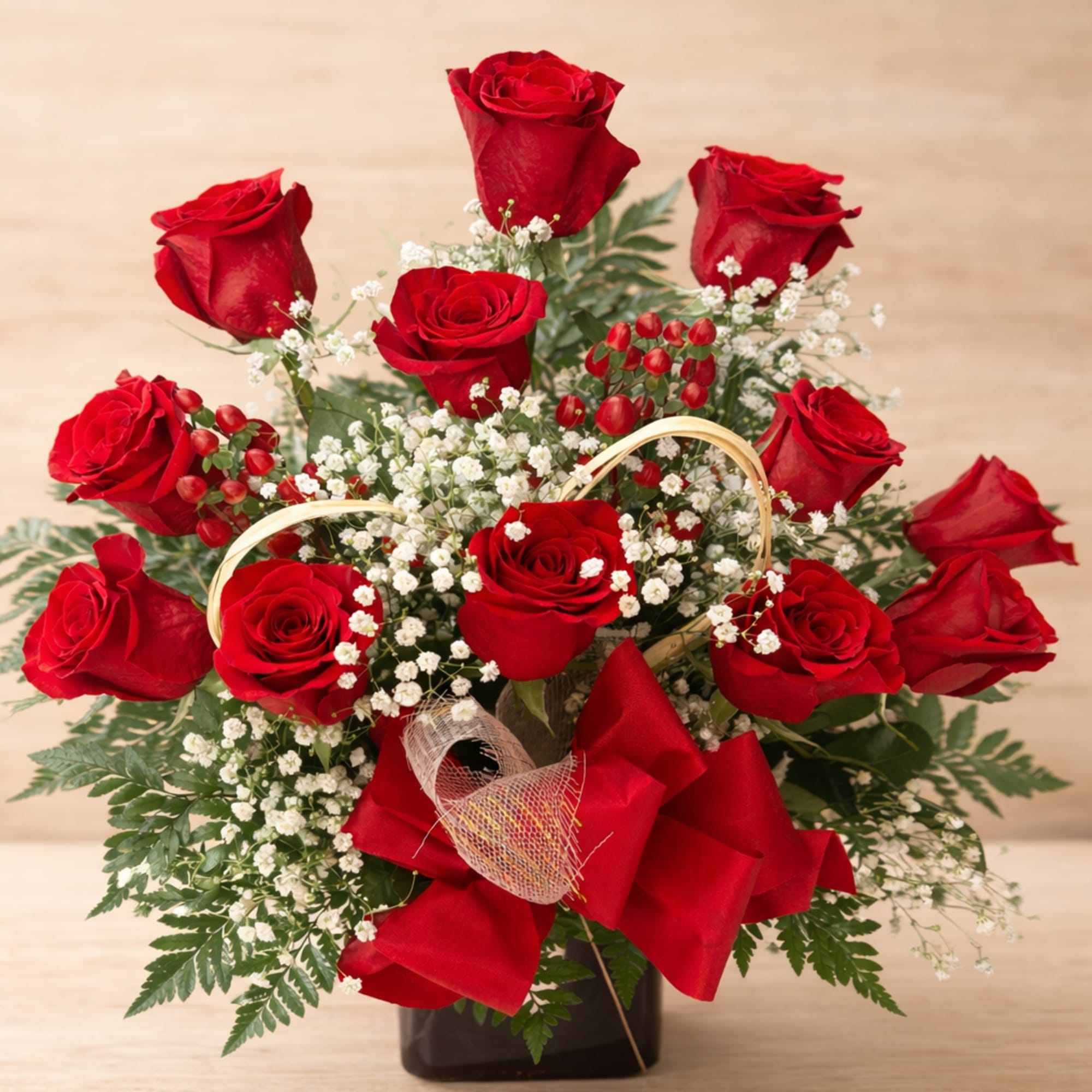 Red roses arranged in a black vase with baby's breath and a red ribbon