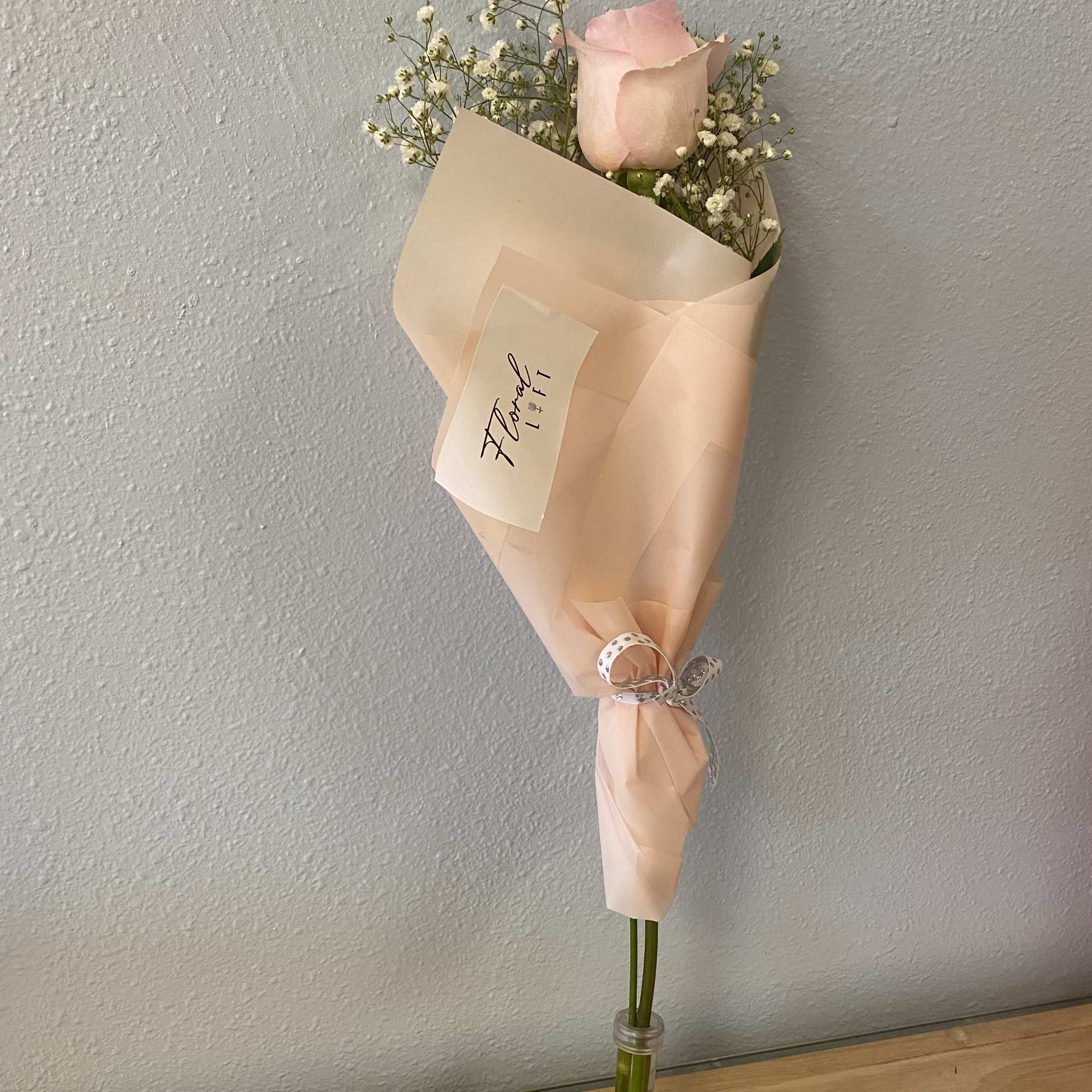 Single pink rose wrapped in peach paper with baby's breath