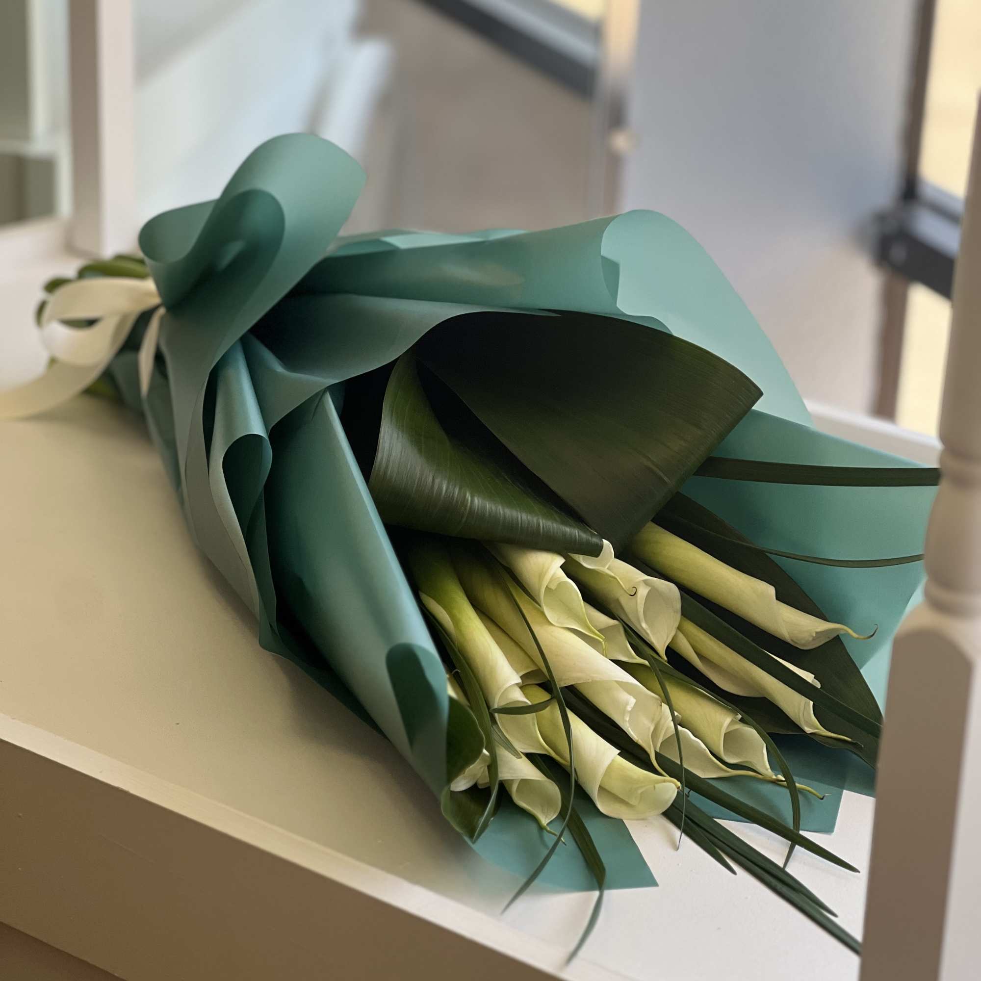 Bouquet of white calla lilies wrapped in teal paper