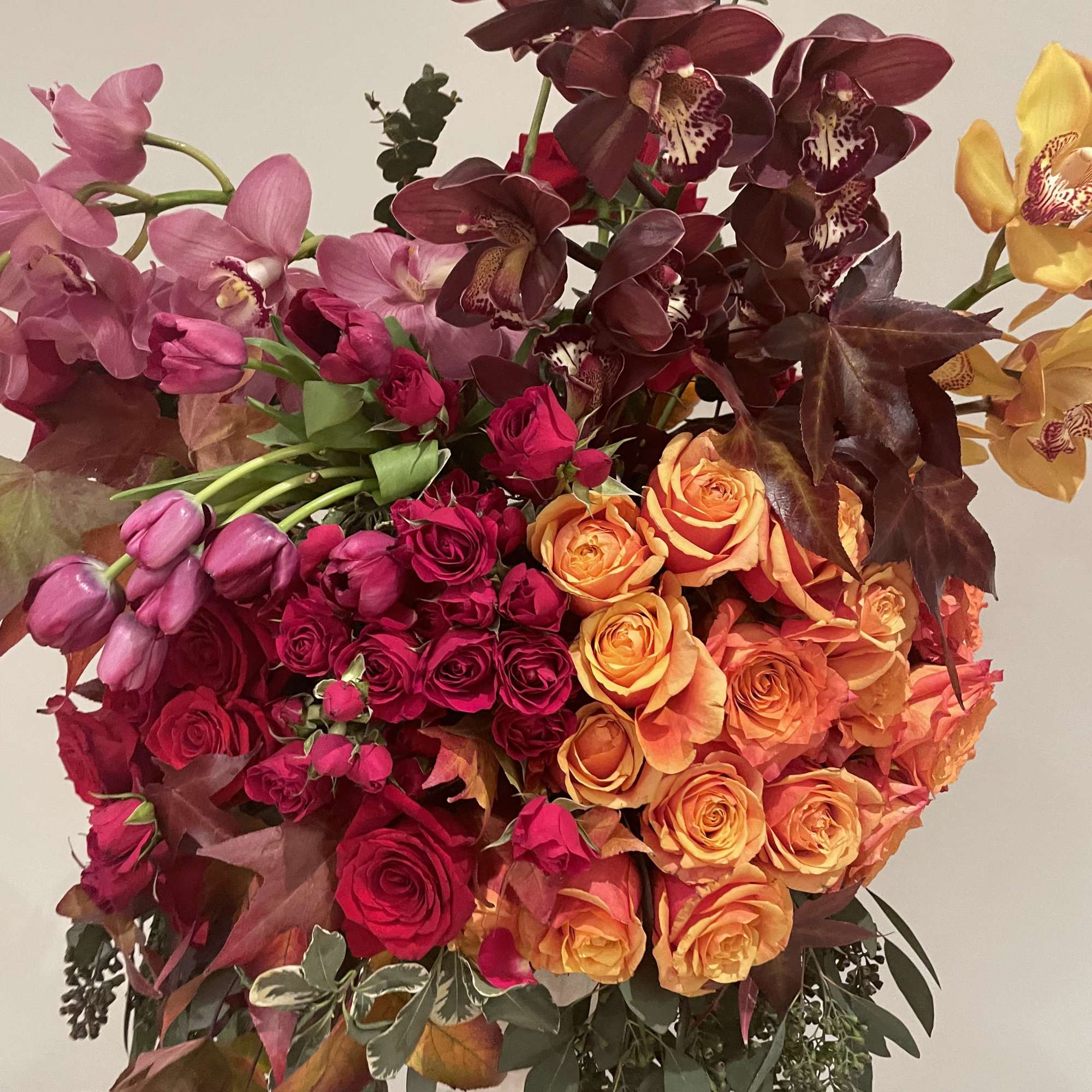 Large bouquet of orchids and roses in pink, orange, and burgundy