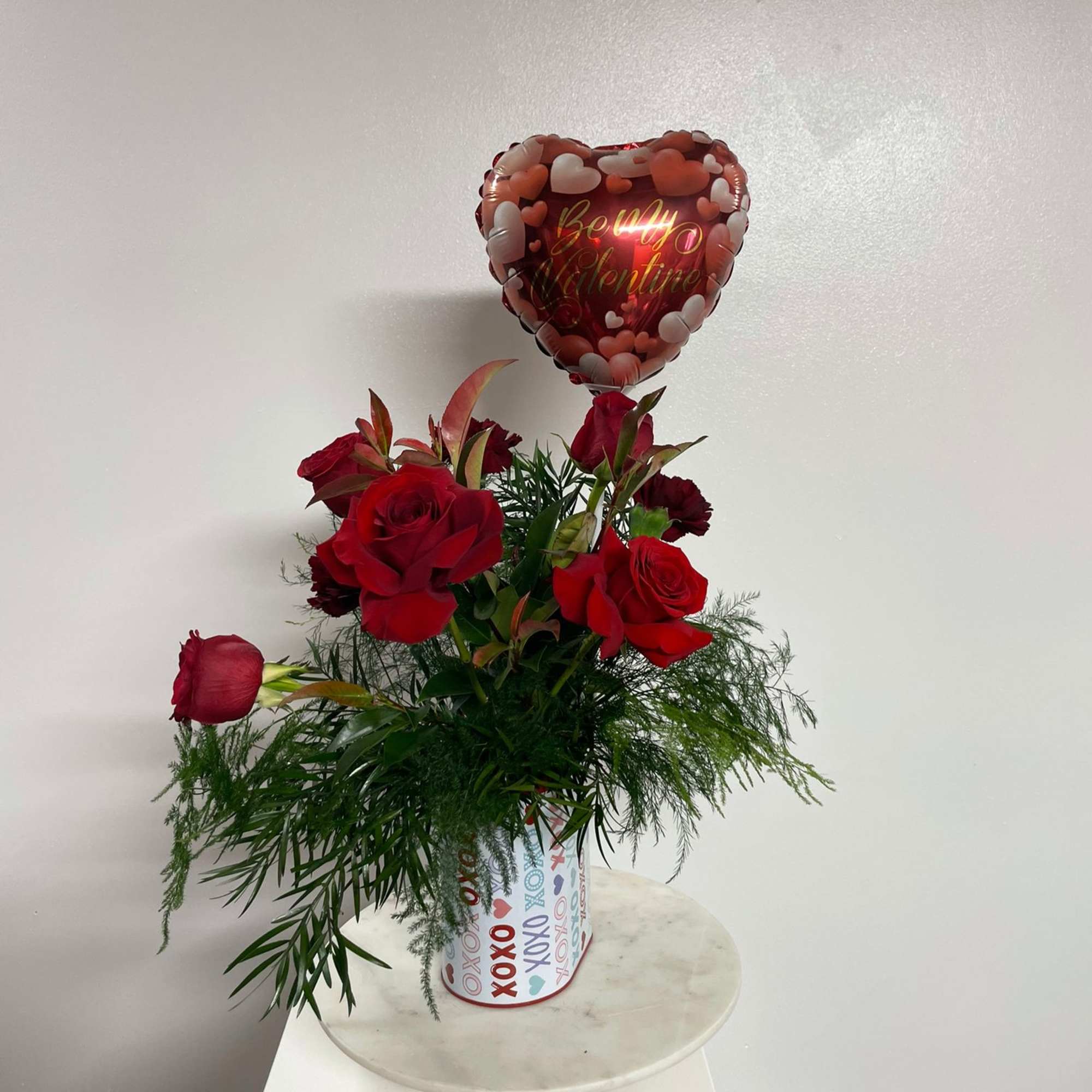 Red roses in a decorated container with a heart balloon above