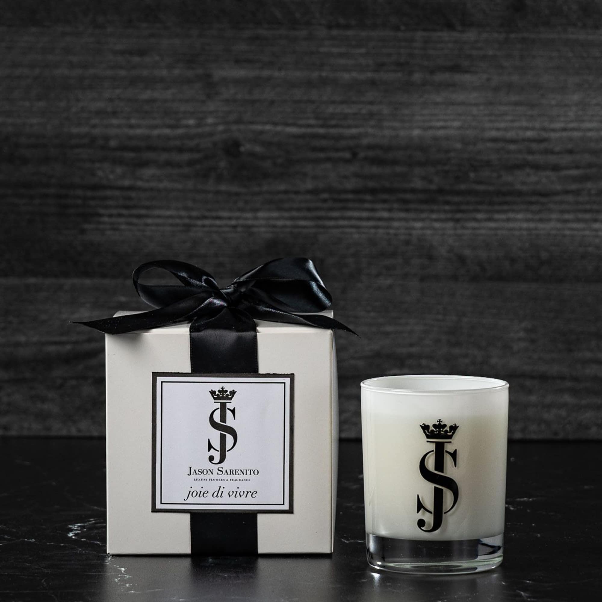 White gift box with black ribbon beside a white candle in a glass holder