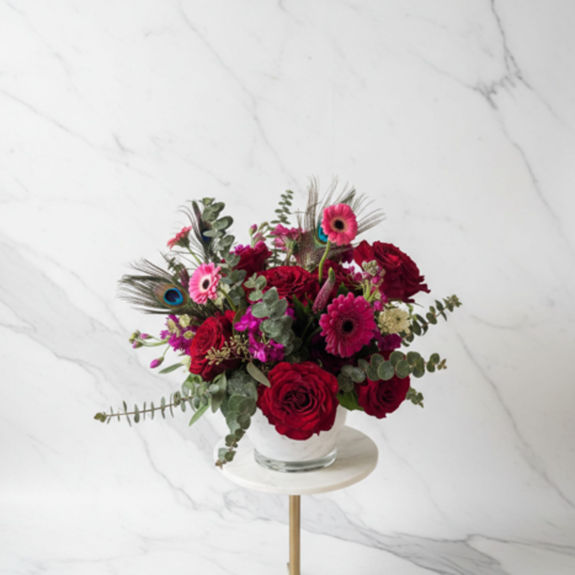Red and pink flower arrangement in a clear glass vase on a stand